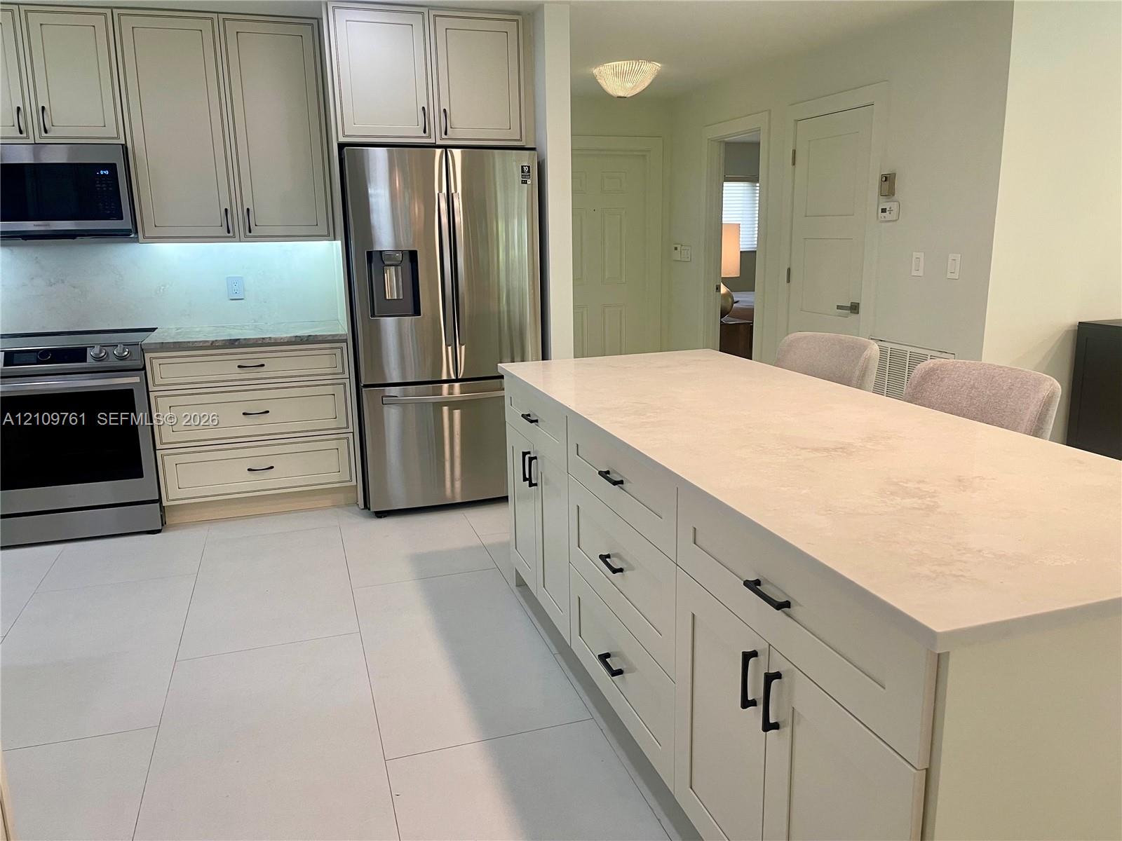 Kitchen featuring an expansive central island with stone-finish countertops, stainless steel appliances, shaker-style cabinetry, and large-format tile flooring