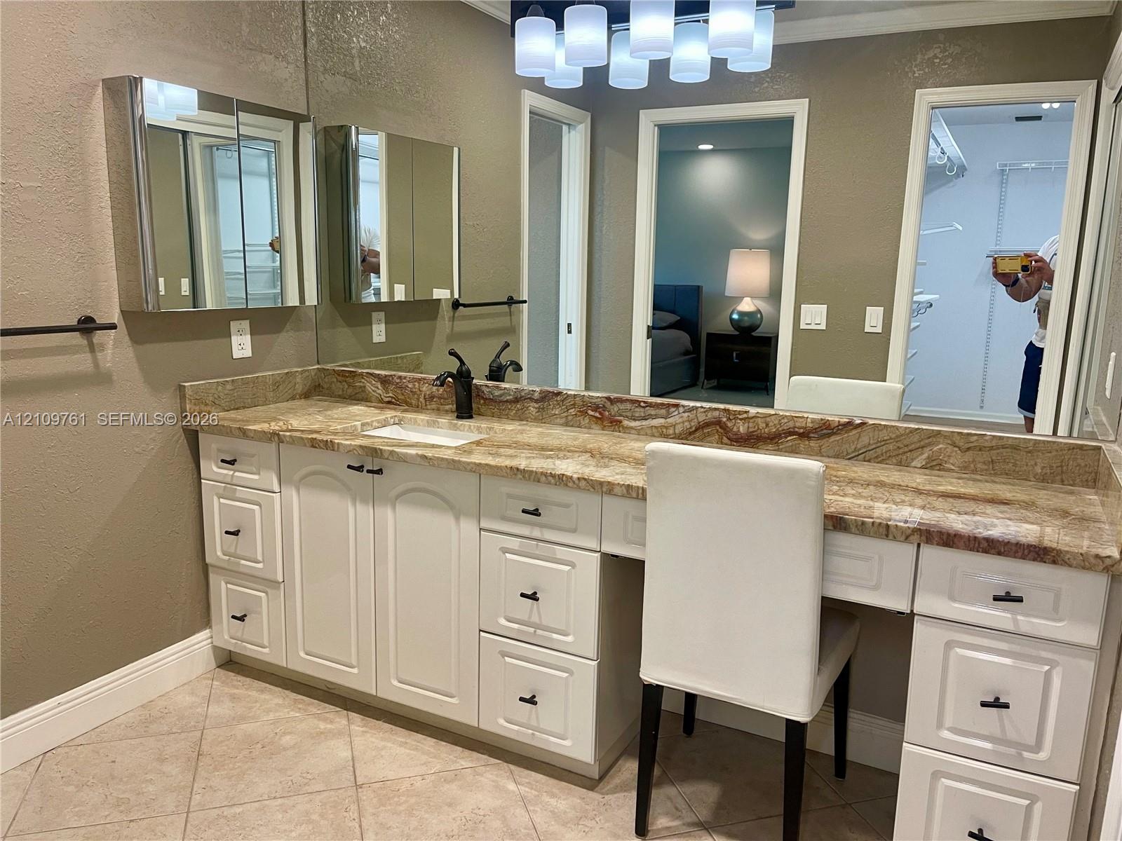 Extended vanity featuring white cabinetry, stone-surface countertop, dual medicine cabinets, multi-light fixture, and ceramic tile flooring