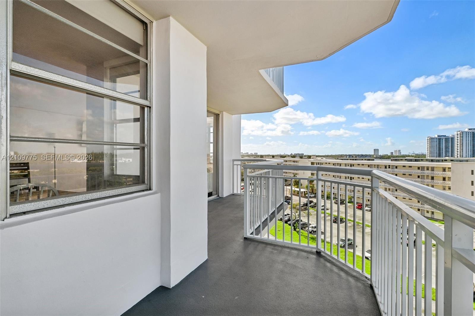Covered balcony featuring white metal railings, smooth concrete flooring, and large-format sliding glass doors