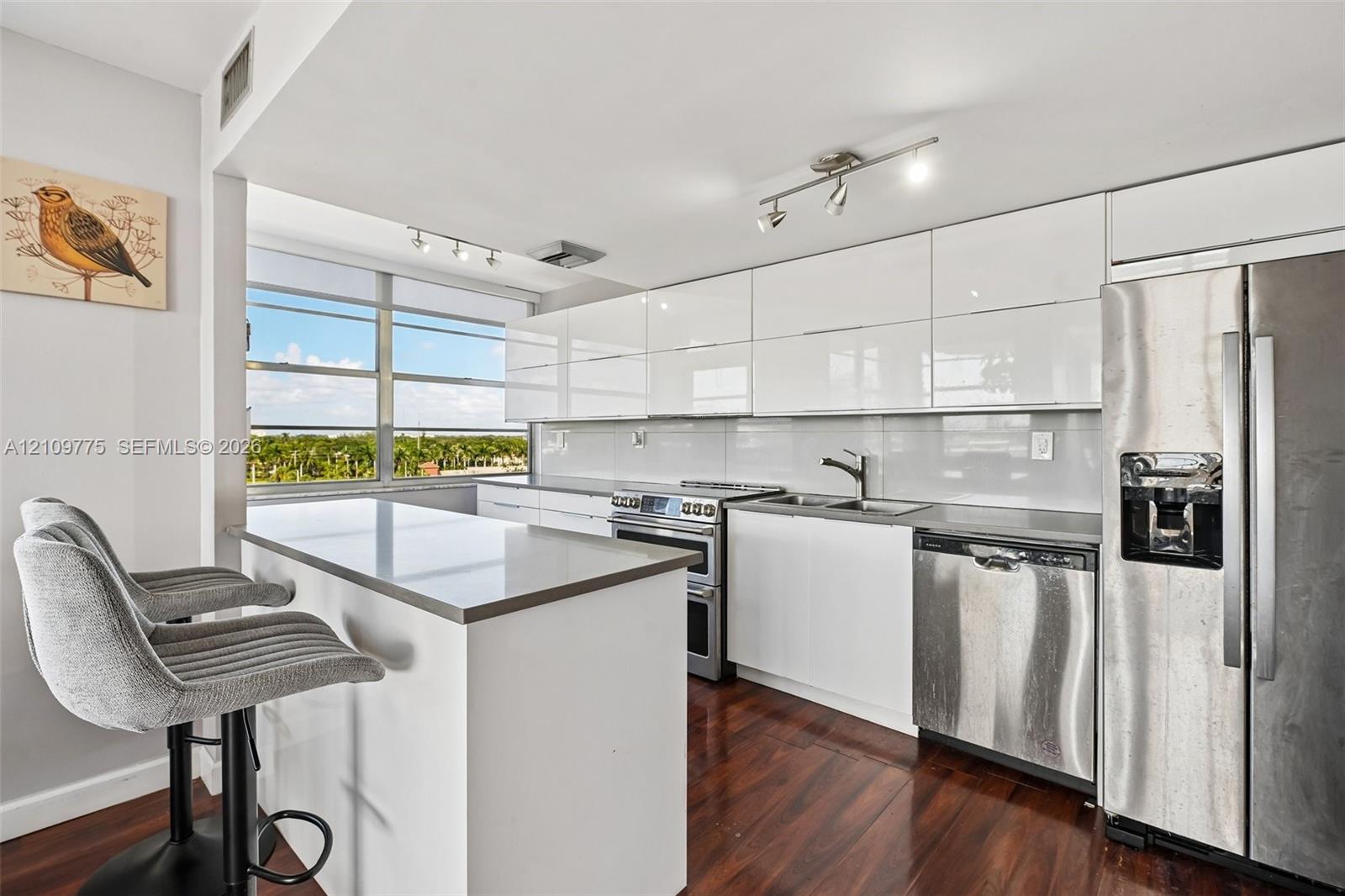 Kitchen featuring high-gloss white cabinetry, stone-finish countertops, stainless steel appliances, track lighting, and wood-finish flooring