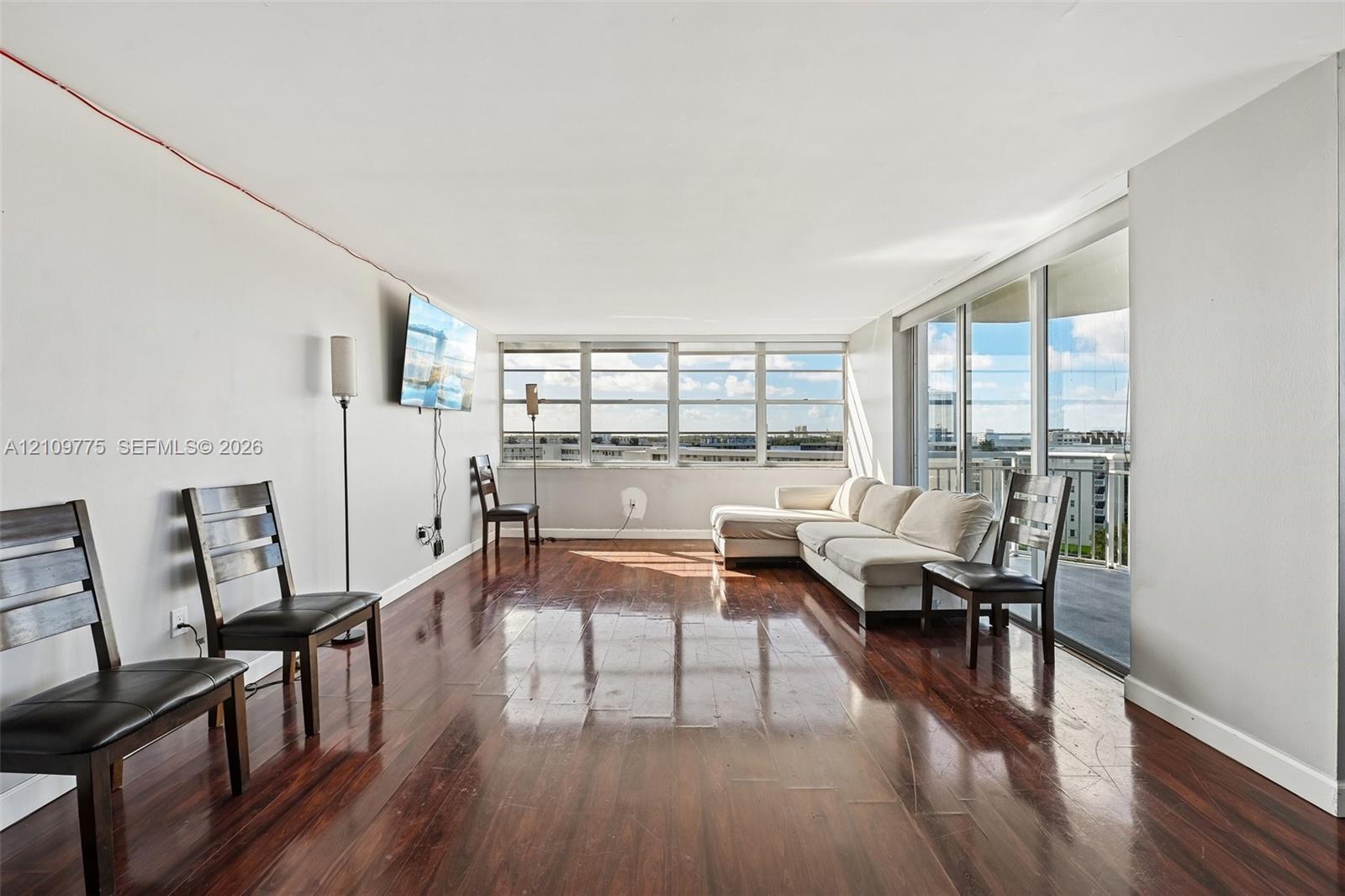 Expansive living area featuring wood-finish flooring, floor-to-ceiling windows, and a sliding glass door providing access to a balcony