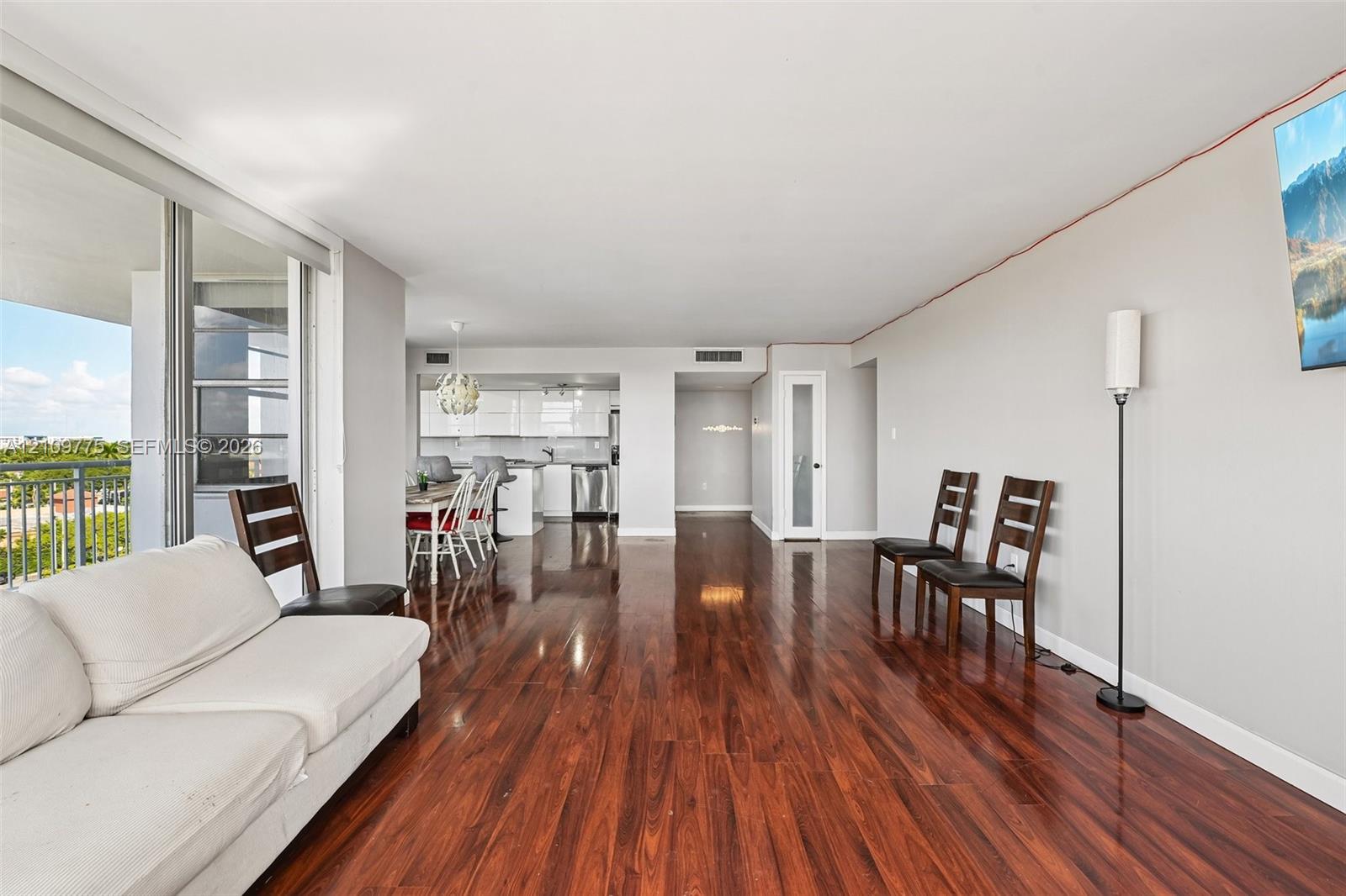Open-concept living space featuring wood-finish flooring, floor-to-ceiling glass sliding doors, recessed ceiling lighting, and a kitchen equipped with high-gloss cabinetry and stainless steel appliances