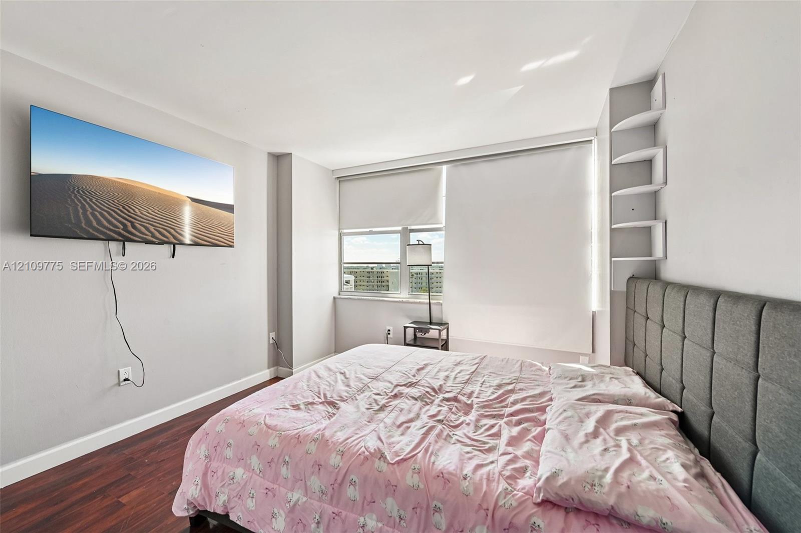 Room featuring wood-finish flooring, multi-pane window with integrated roller shades, and built-in corner shelving