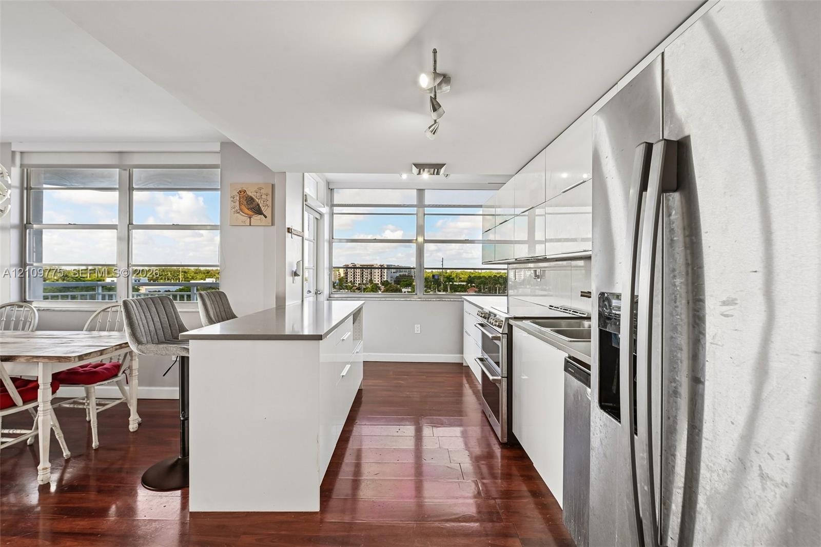 Kitchen featuring high-gloss white cabinetry, stainless steel appliances, solid-surface countertops, a breakfast bar, and wood-finish flooring