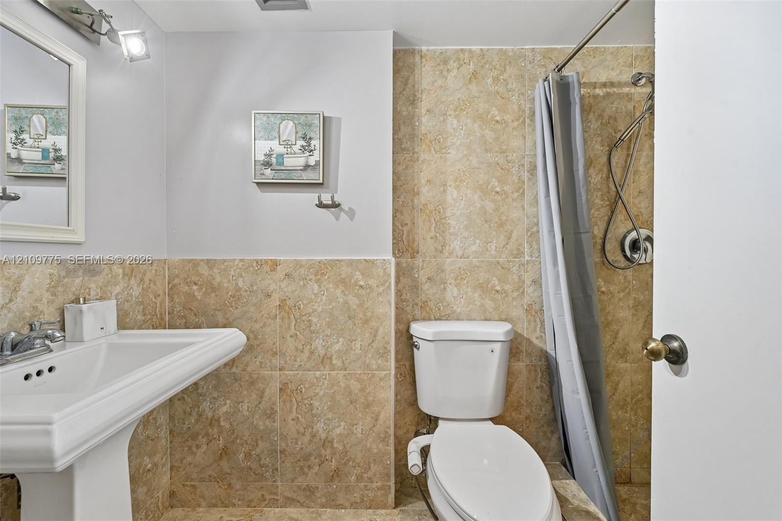 Pedestal sink with chrome faucet, wall-mounted vanity mirror, and floor-to-ceiling neutral-toned tile shower enclosure