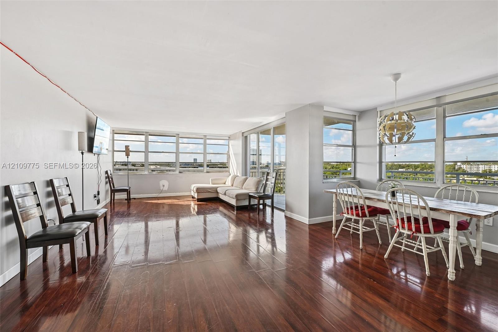 Expansive open-concept living area featuring polished wood-finish flooring, floor-to-ceiling windows, and a built-in overhead light fixture