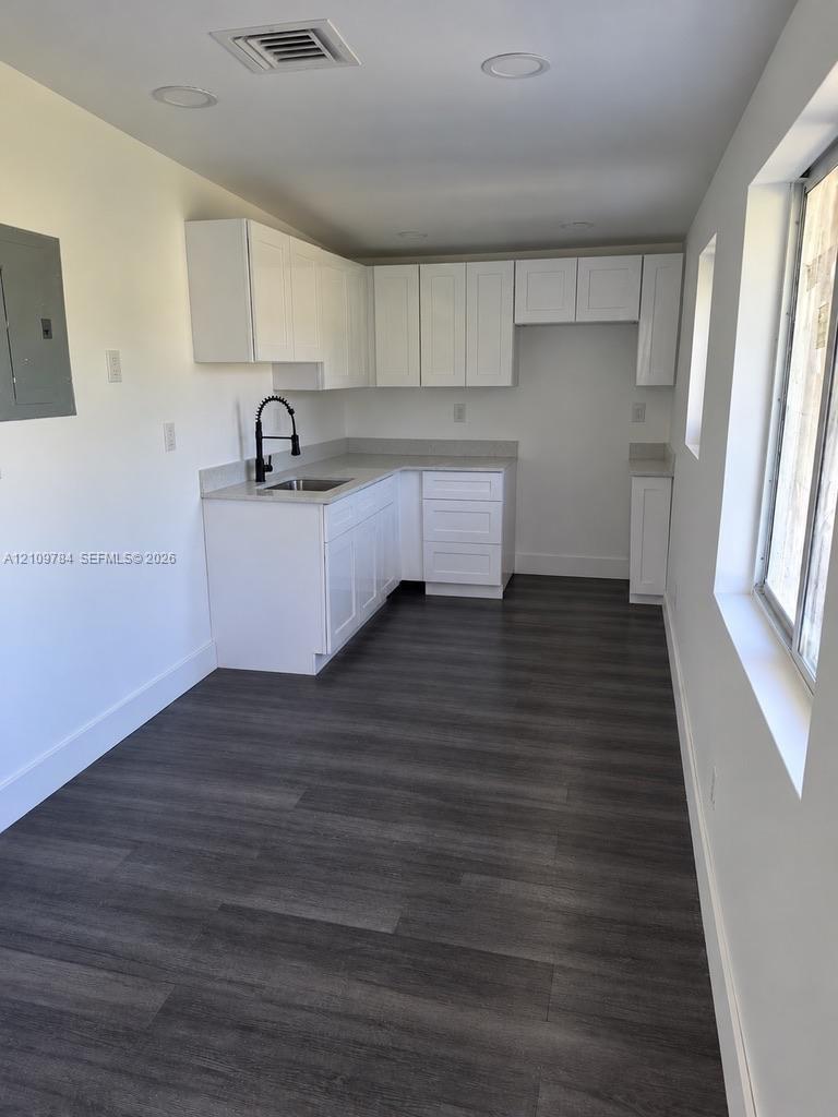 White shaker-style cabinetry, neutral stone-finish countertops, wood-finish flooring, recessed lighting, and a matte black gooseneck faucet