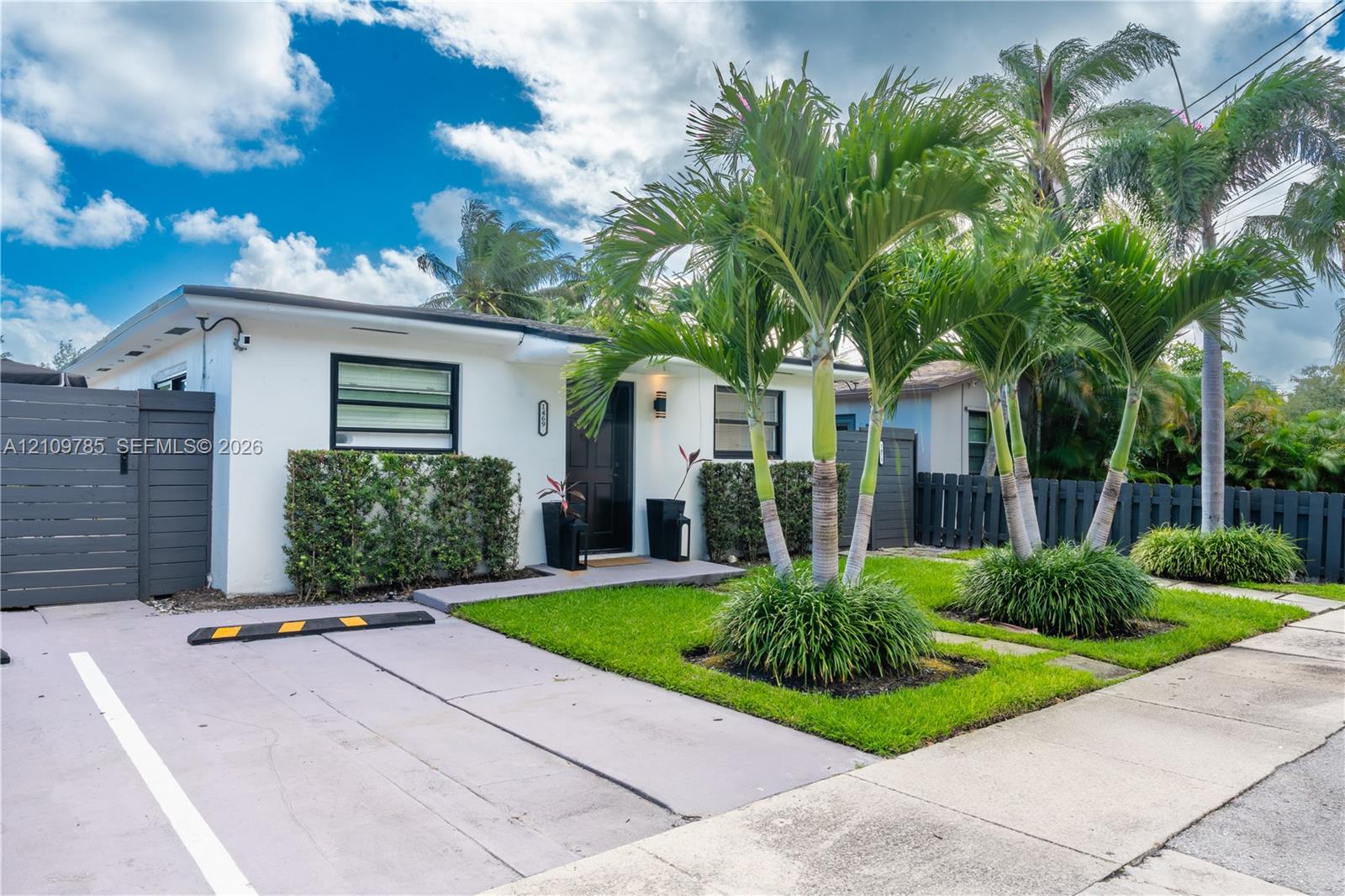 Exterior facade featuring privacy fencing, parking, and curated landscaping with mature palm trees