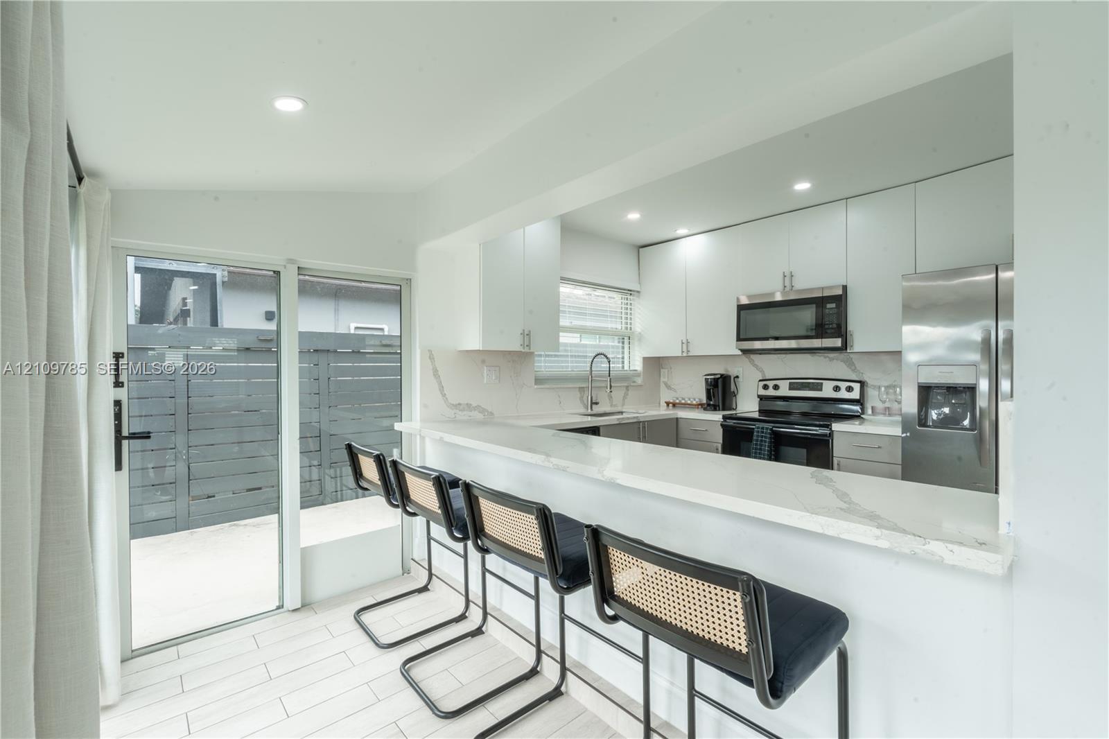 Kitchen featuring flat-panel cabinetry, stone-finish countertops with waterfall edge, stainless steel appliances, and large-format tile flooring