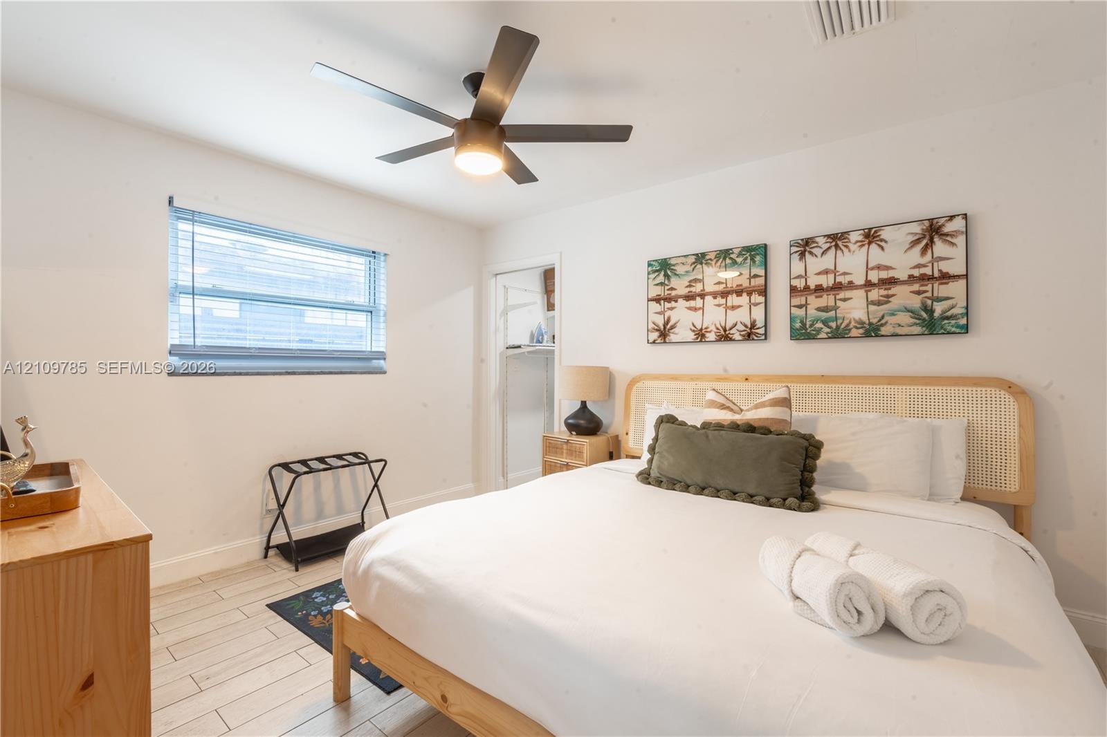 Room featuring white walls, light-toned wood-finish flooring, a multi-blade ceiling fan with integrated lighting, and a horizontal window with blinds