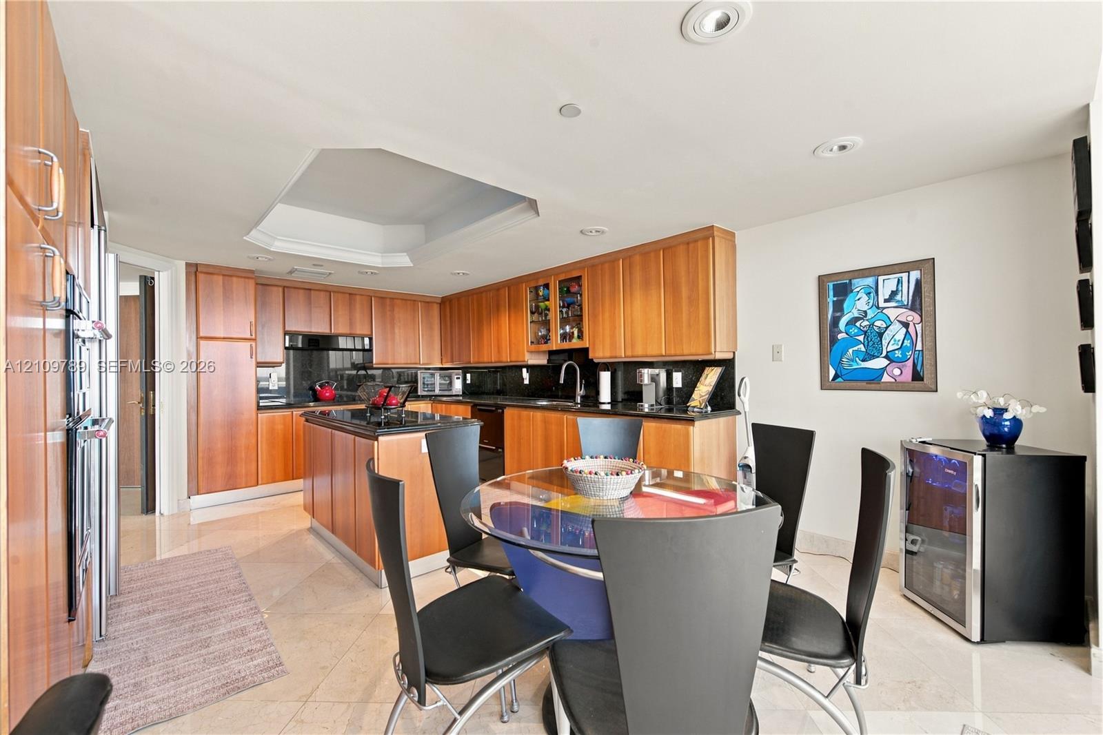 Kitchen featuring wood-veneer cabinetry, stone countertops, central island, recessed ceiling lighting, and polished stone flooring