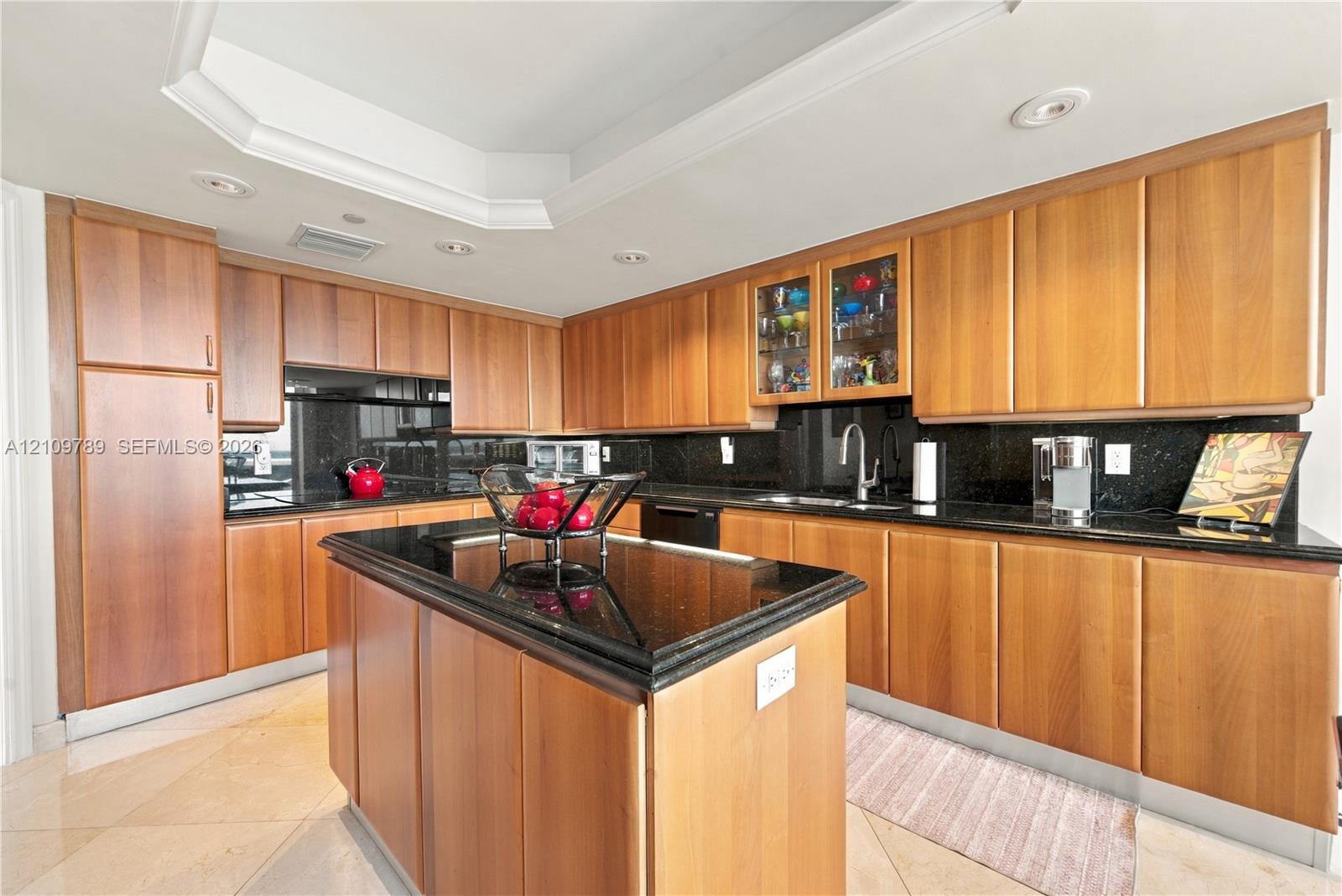 Kitchen featuring wood cabinetry, black countertops, central island, tray ceiling, and recessed lighting