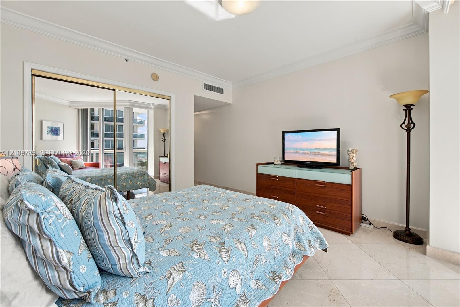 Bedroom featuring neutral walls, crown molding, polished tile flooring, and a mirrored sliding-door closet