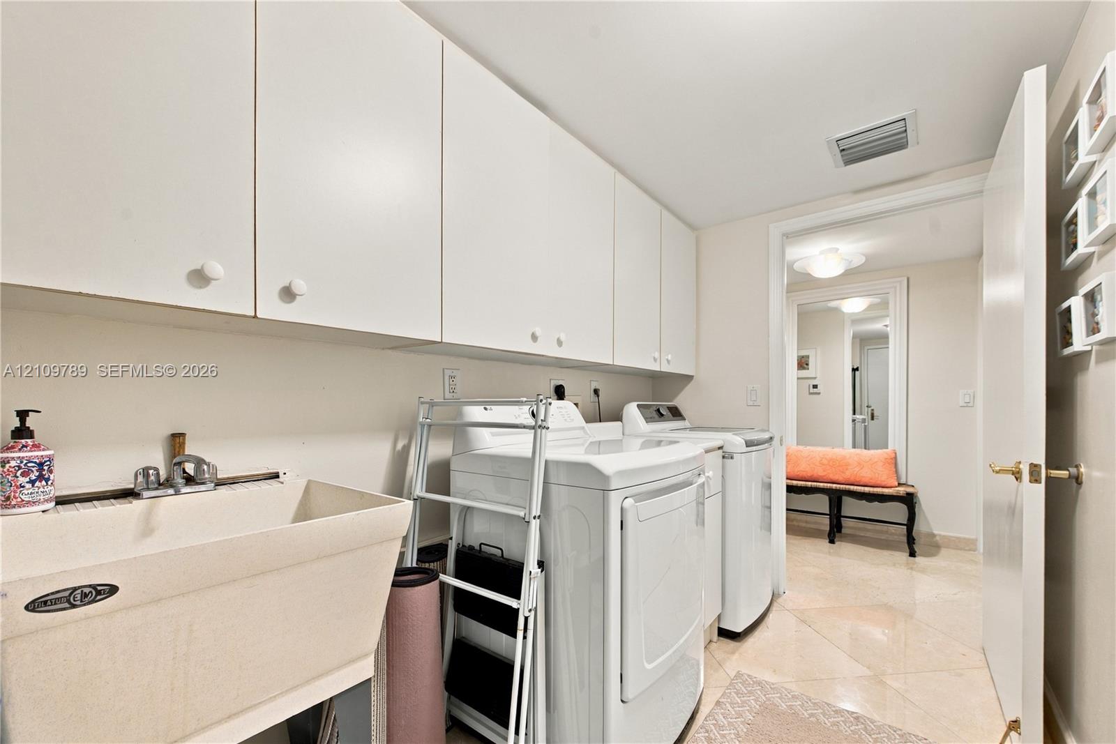 Laundry area featuring white flat-panel upper cabinetry, a deep basin utility sink with a chrome faucet, and tile flooring