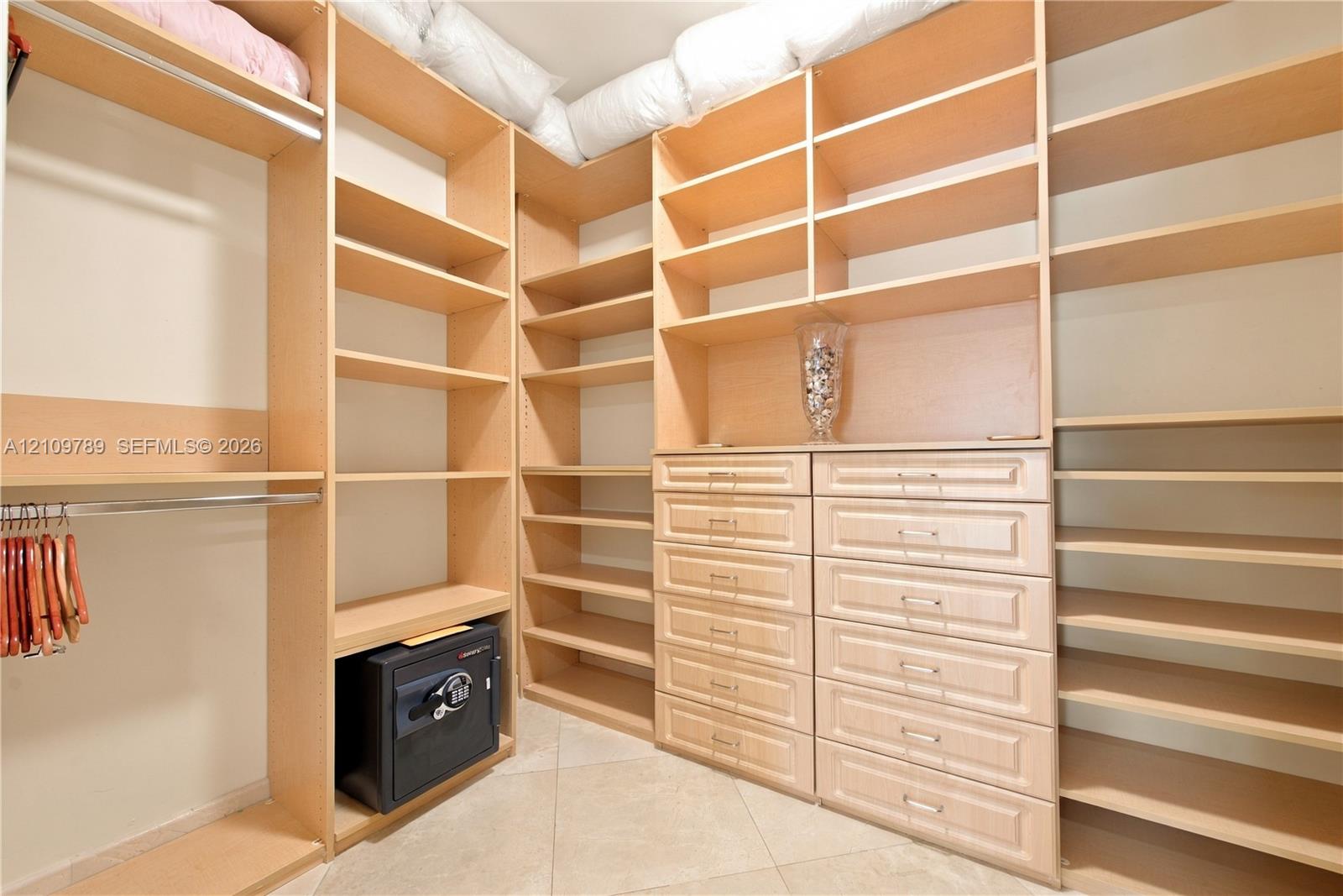 Walk-in closet featuring light wood-finish built-in shelving, integrated dresser drawers with metal hardware, and dual clothing rods