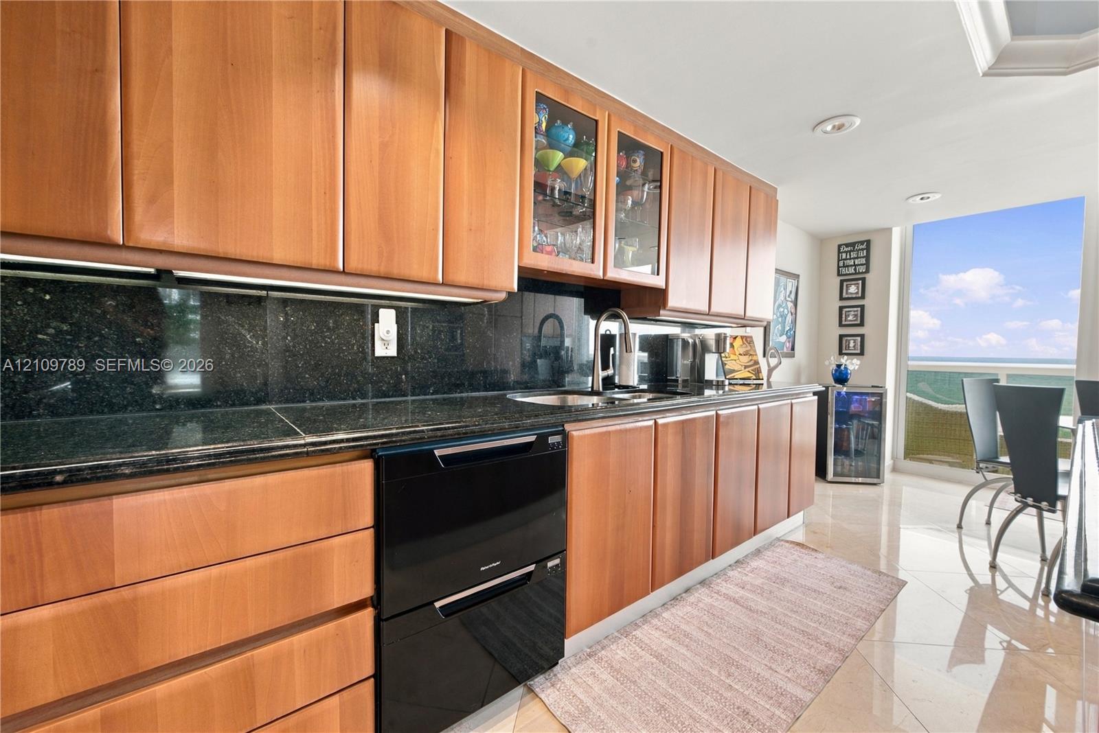 Kitchen featuring flat-panel wood cabinetry, dark stone countertops, an integrated dishwasher, glass-front upper cabinet doors, and recessed lighting