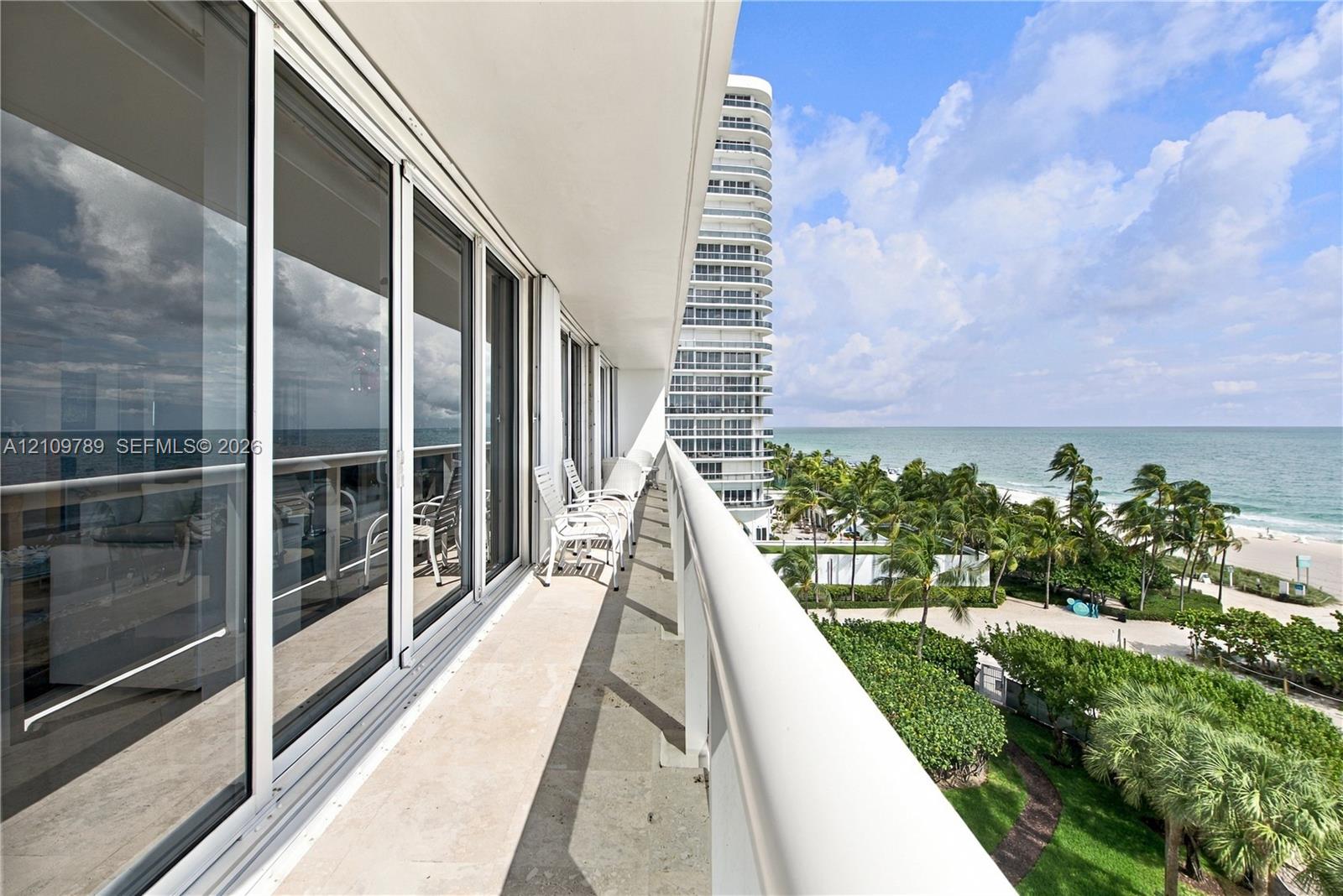 Covered balcony featuring stone flooring, a white metal railing, and floor-to-ceiling sliding glass doors
