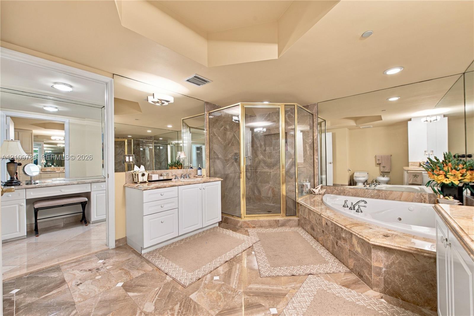 Bathroom featuring stone tile flooring, a built-in vanity with cabinetry, a jetted soaking tub with a stone surround, and a walk-in shower with metal framing