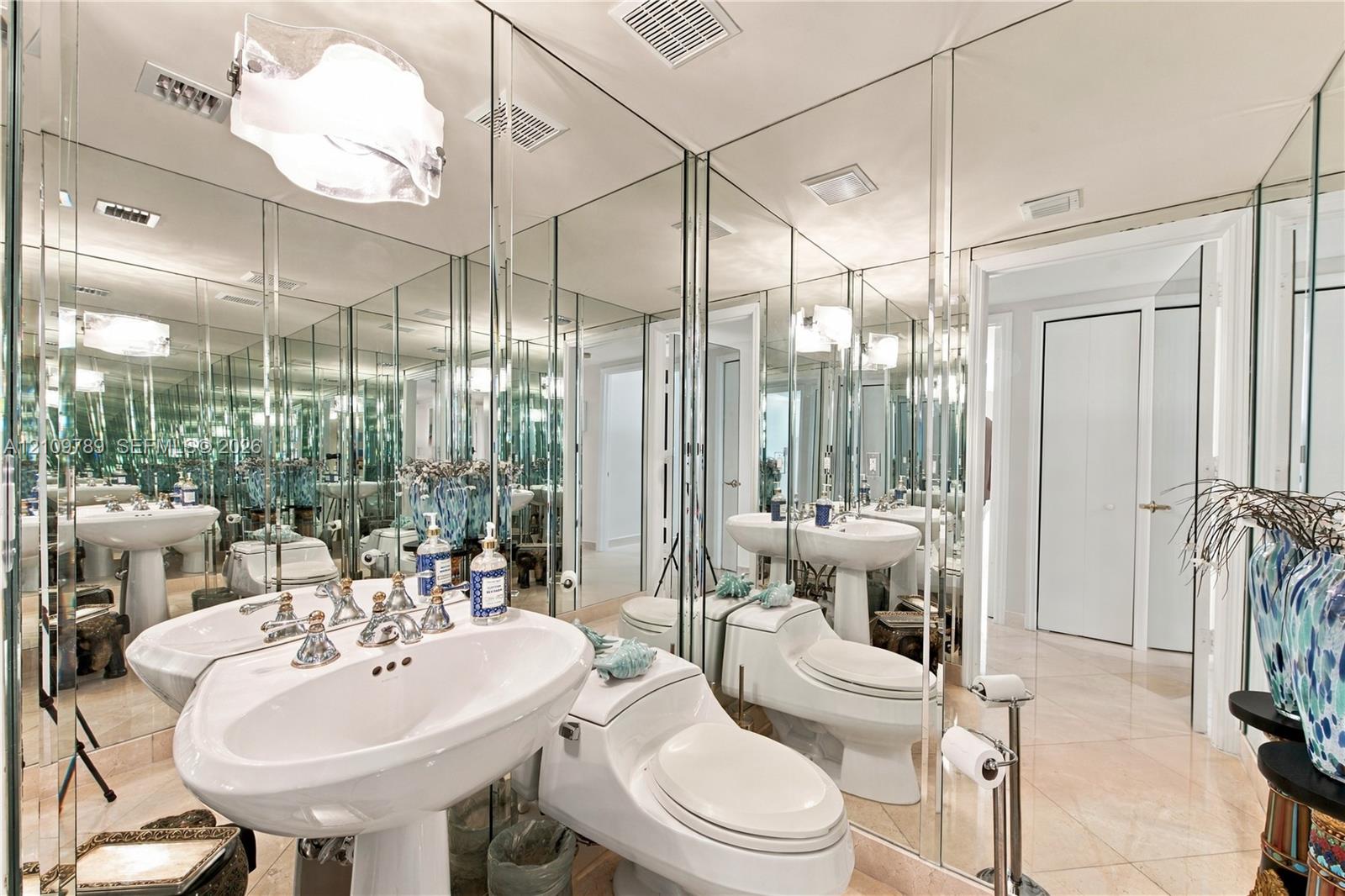 Full-wall vanity mirror, dual porcelain pedestal sinks, polished stone flooring, and contemporary pendant lighting