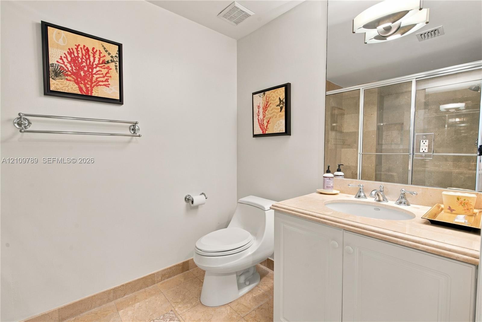 Bathroom featuring a vanity with a stone-top integrated sink, a glass-enclosed shower, wall-to-wall mirror, polished chrome hardware, and tile flooring