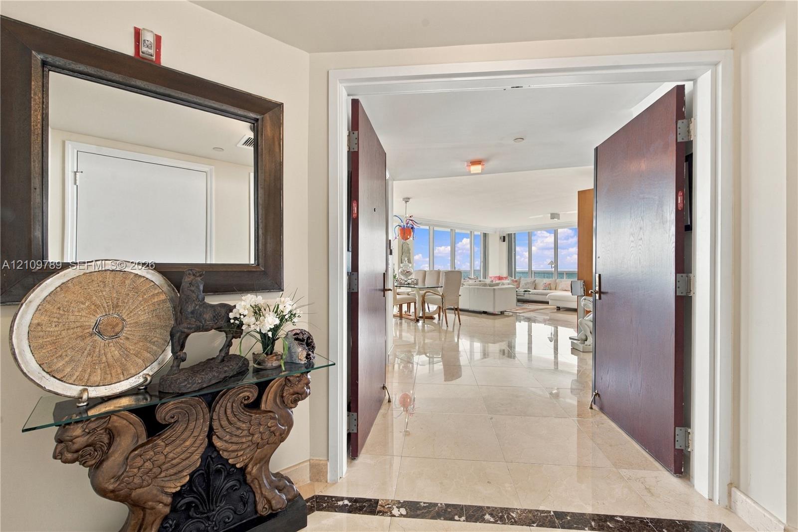 Foyer entrance featuring dual solid-core doors, polished stone flooring with a decorative dark stone inlay, and floor-to-ceiling windows