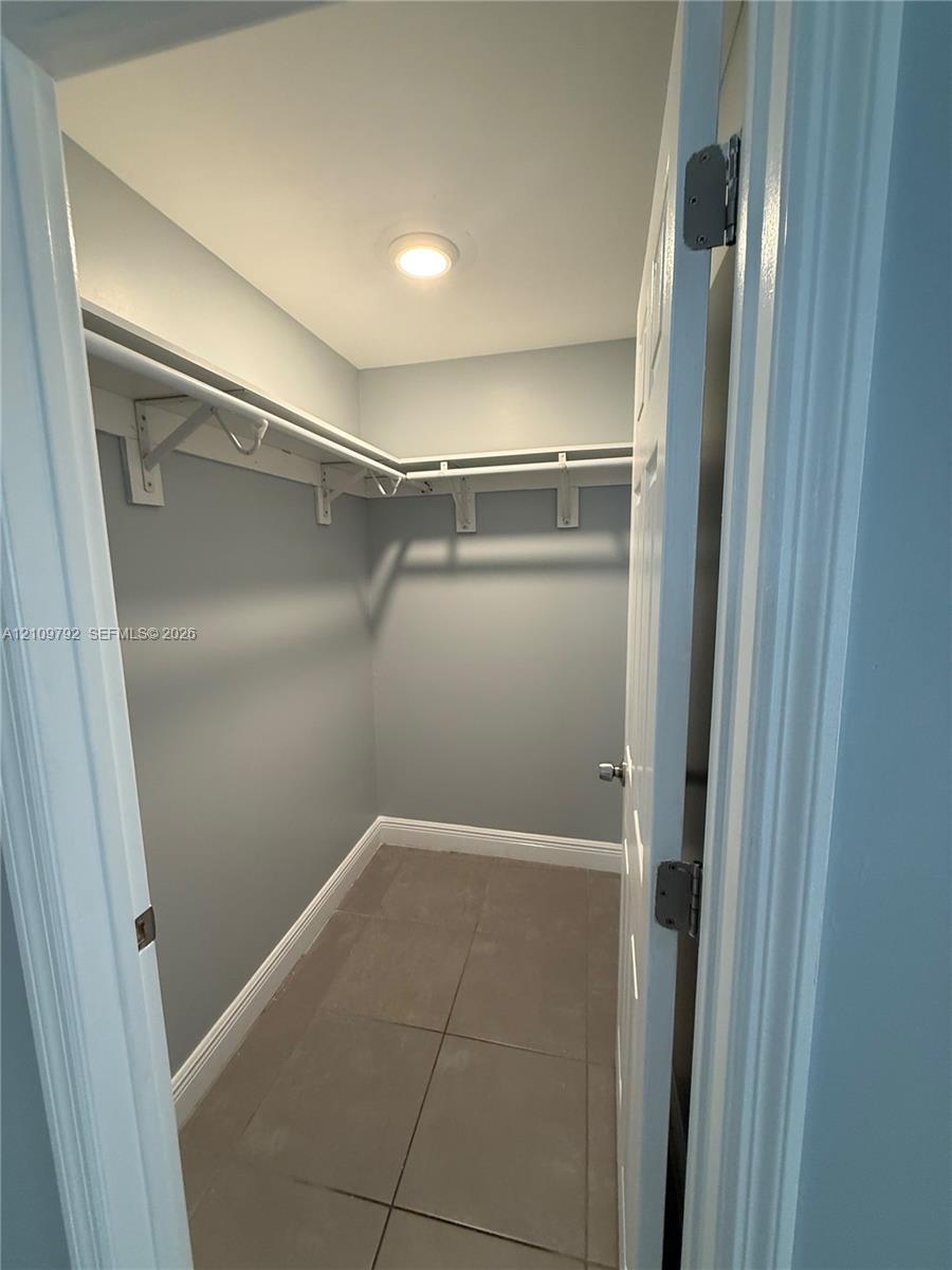 Walk-in closet featuring large-format tile flooring, built-in shelving, and overhead lighting