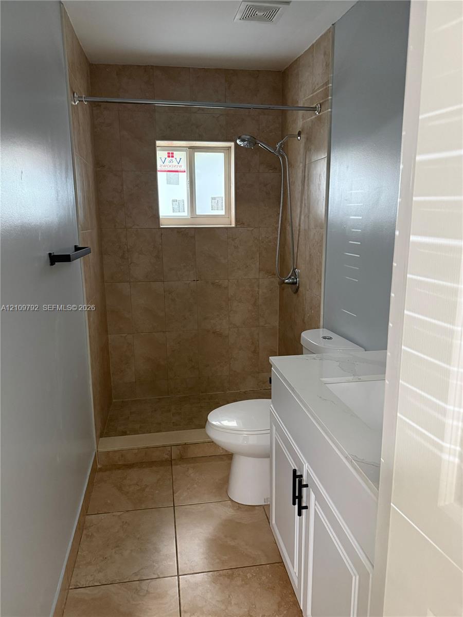 Bathroom featuring tile flooring, walk-in shower with tiled surround, white vanity cabinet with stone-finish countertop, and matte black hardware