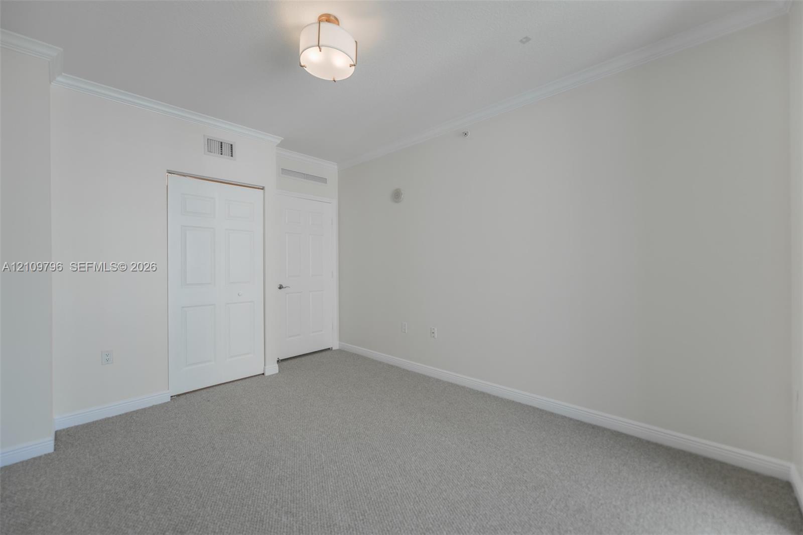 Interior space featuring neutral wall tones, crown molding, wall-to-wall carpeting, a semi-flush mount light fixture, and a multi-panel closet door