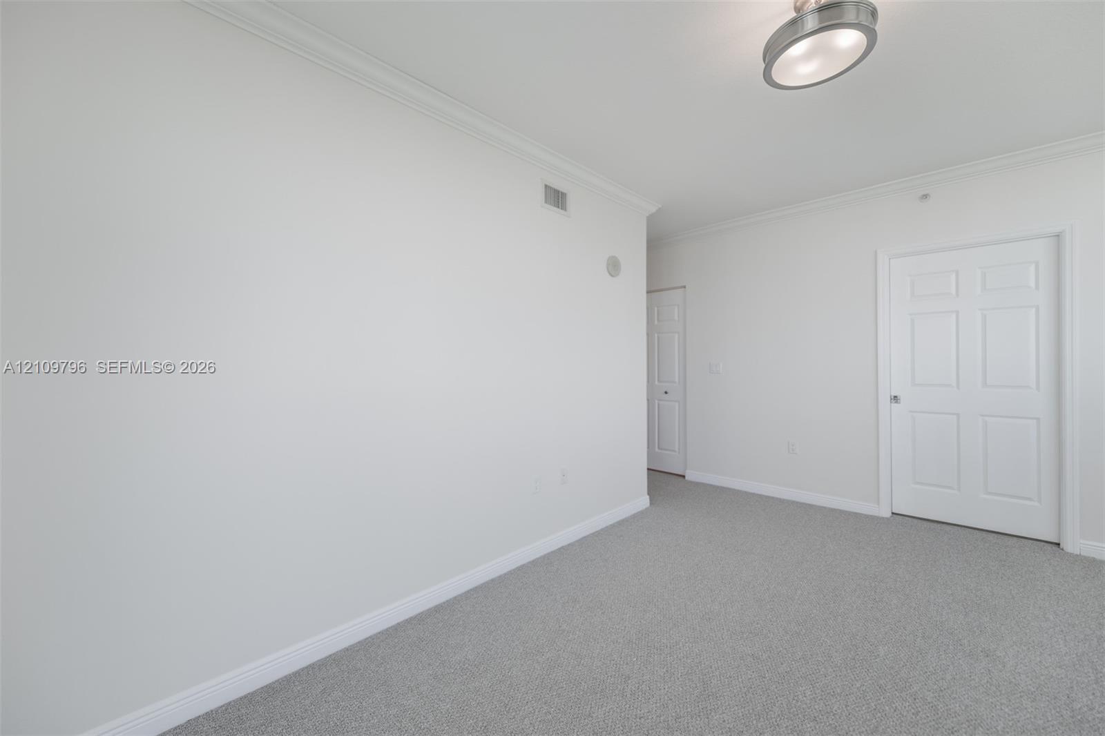 Neutral-toned interior space featuring wall-to-wall carpeting, crown molding, a semi-flush mount ceiling light fixture, and six-panel interior doors