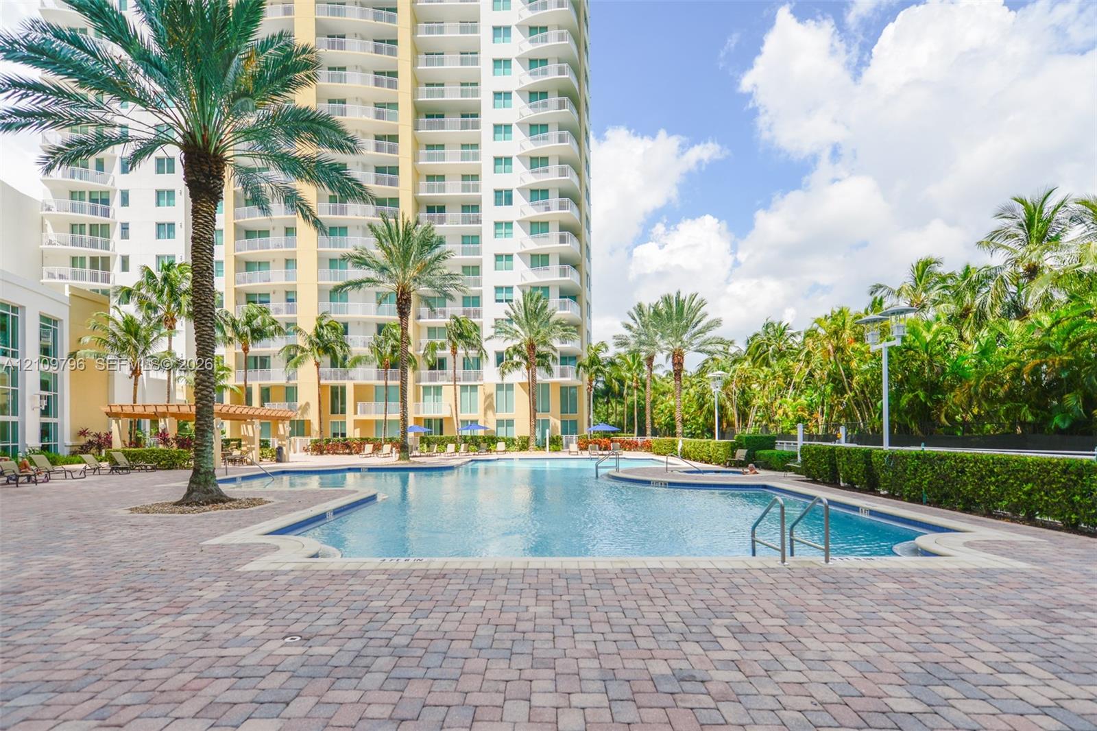 Swimming pool with perimeter paver decking, integrated spa, and mature palm landscaping