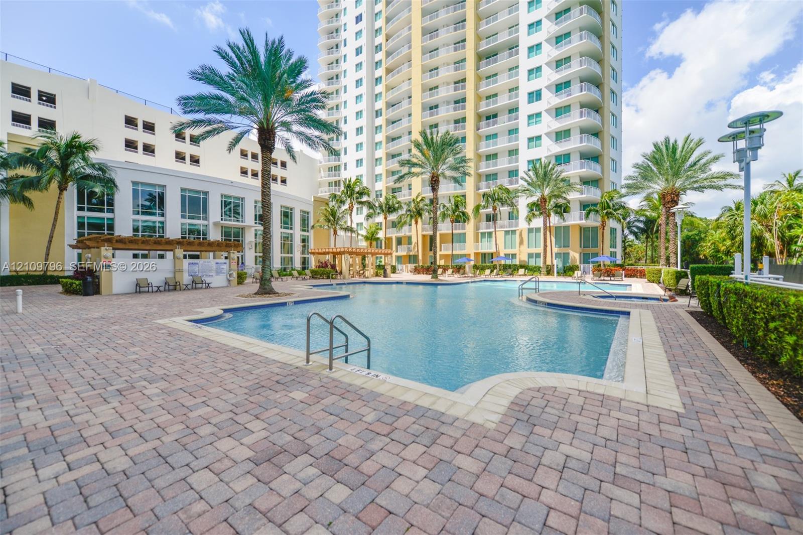 Swimming pool with tile surround, paver decking, attached spa, wooden pergola, and mature palm trees