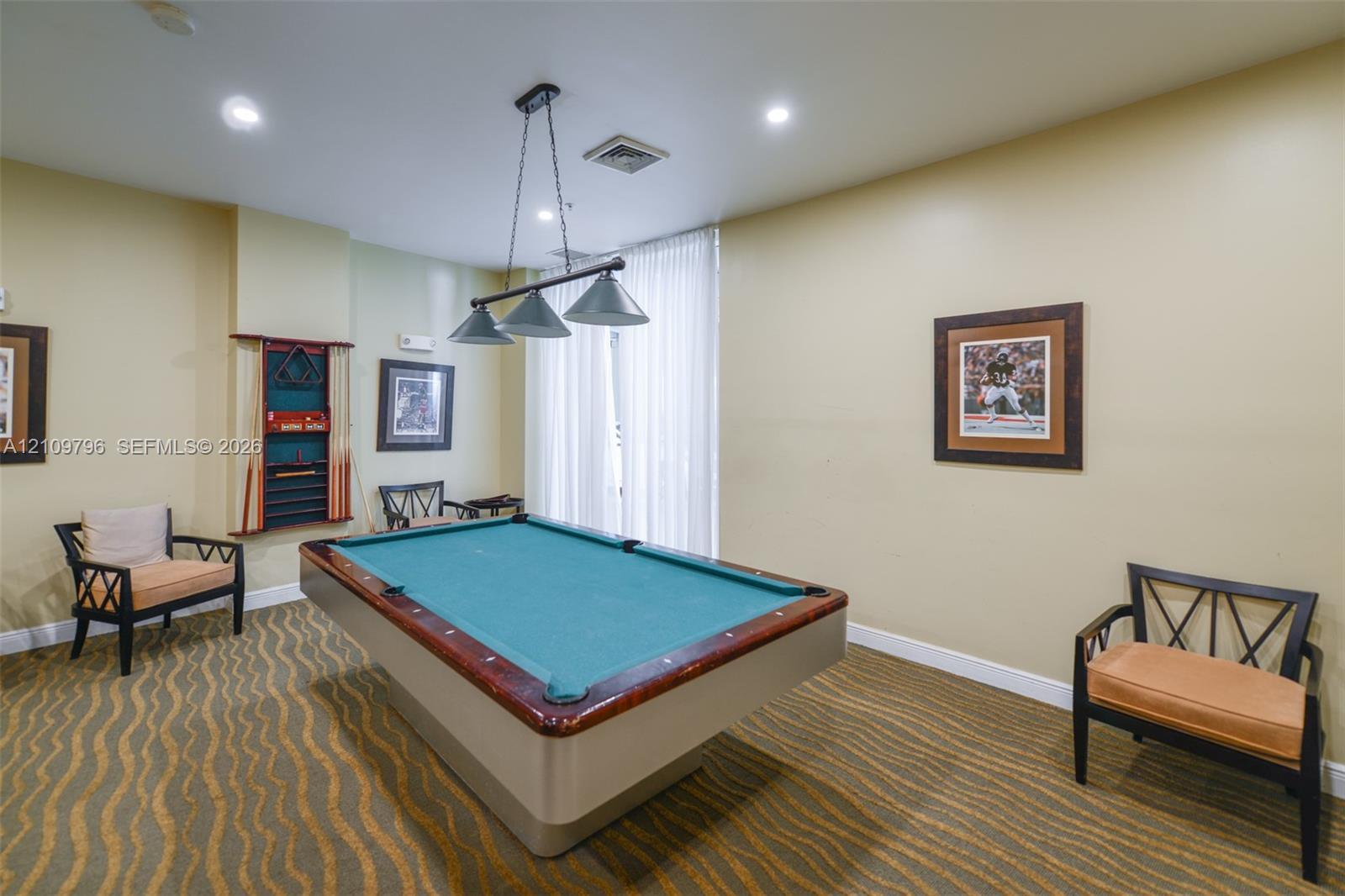 Interior room featuring patterned wall-to-wall carpeting, recessed ceiling lighting, a three-light pendant fixture, and floor-to-ceiling sheer window treatments