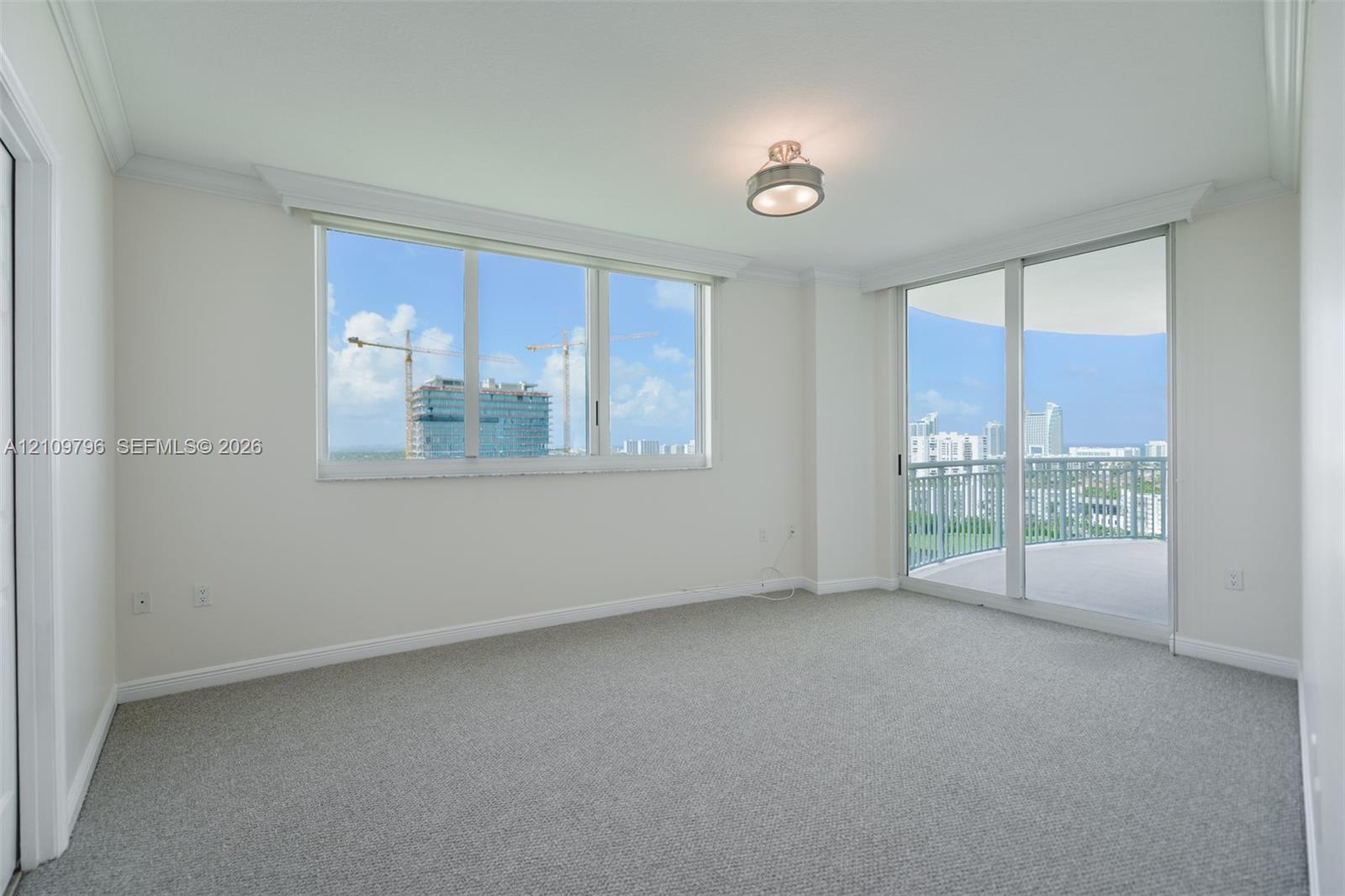 Bright interior space featuring expansive windows, glass sliding doors, neutral carpeting, crown molding, and a private balcony