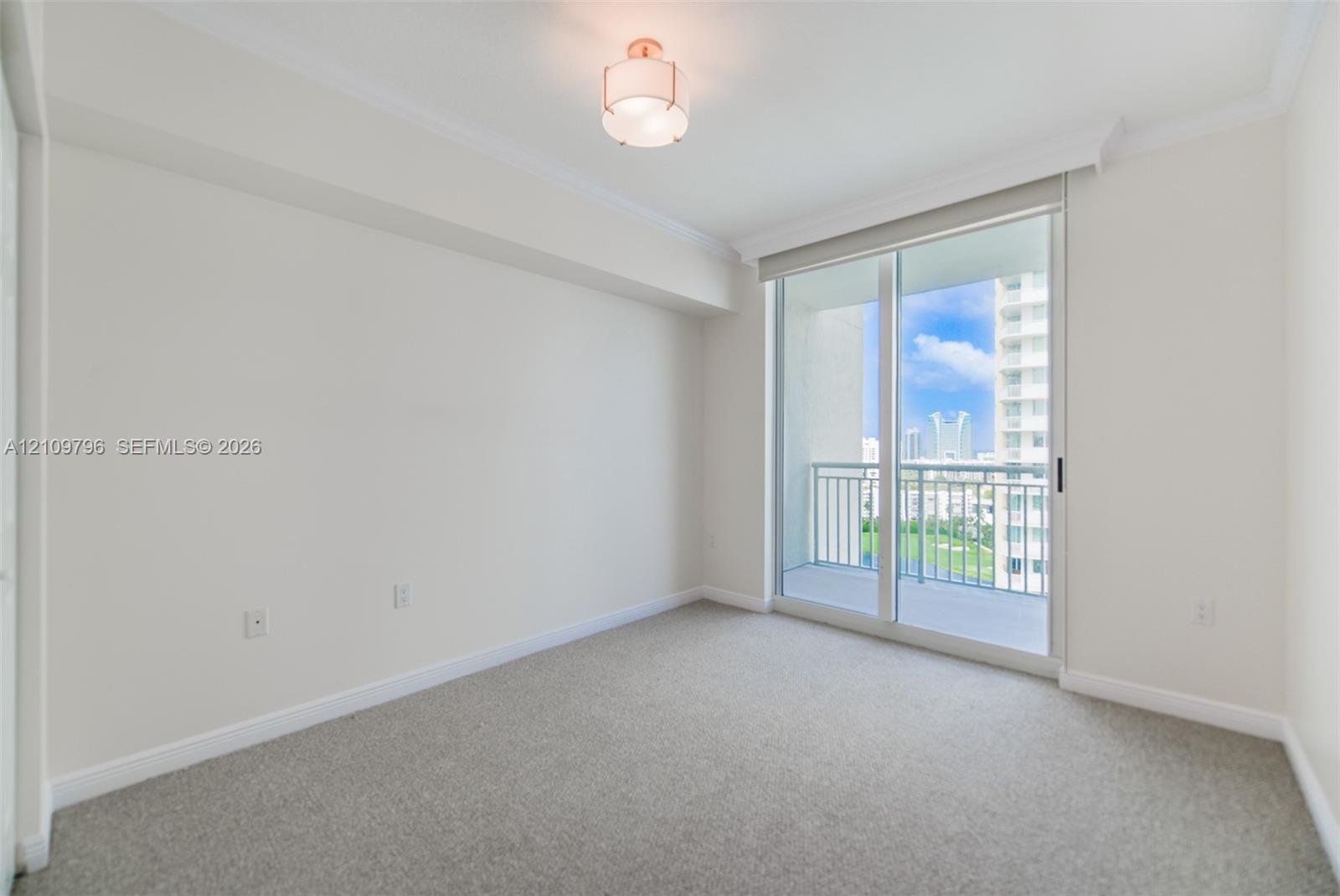Neutral-toned wall-to-wall carpeting, crown molding, drum-style ceiling light fixture, and sliding glass door with access to a balcony