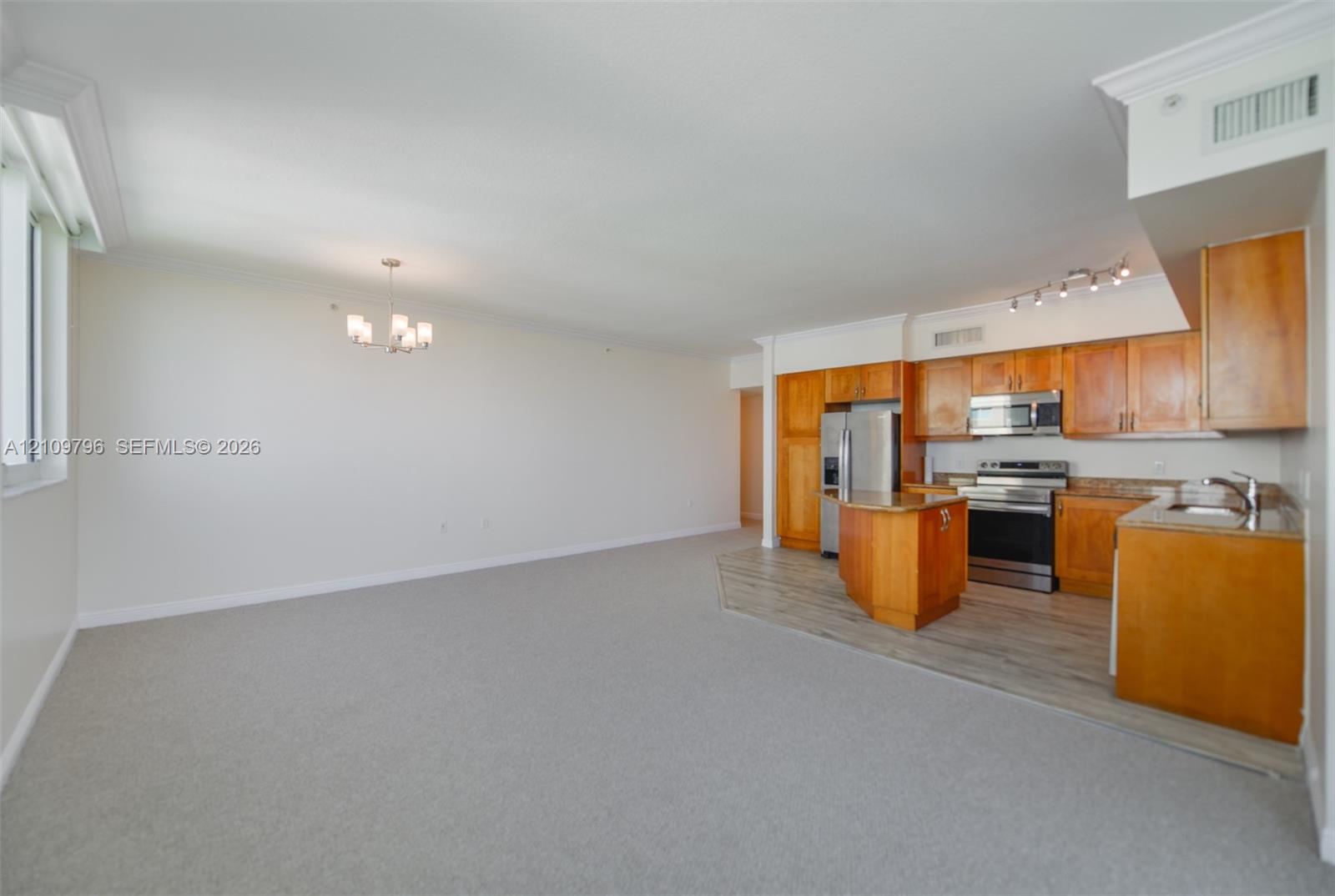 Open-concept space featuring wood-finish cabinetry, stainless steel appliances, a kitchen island, and crown molding