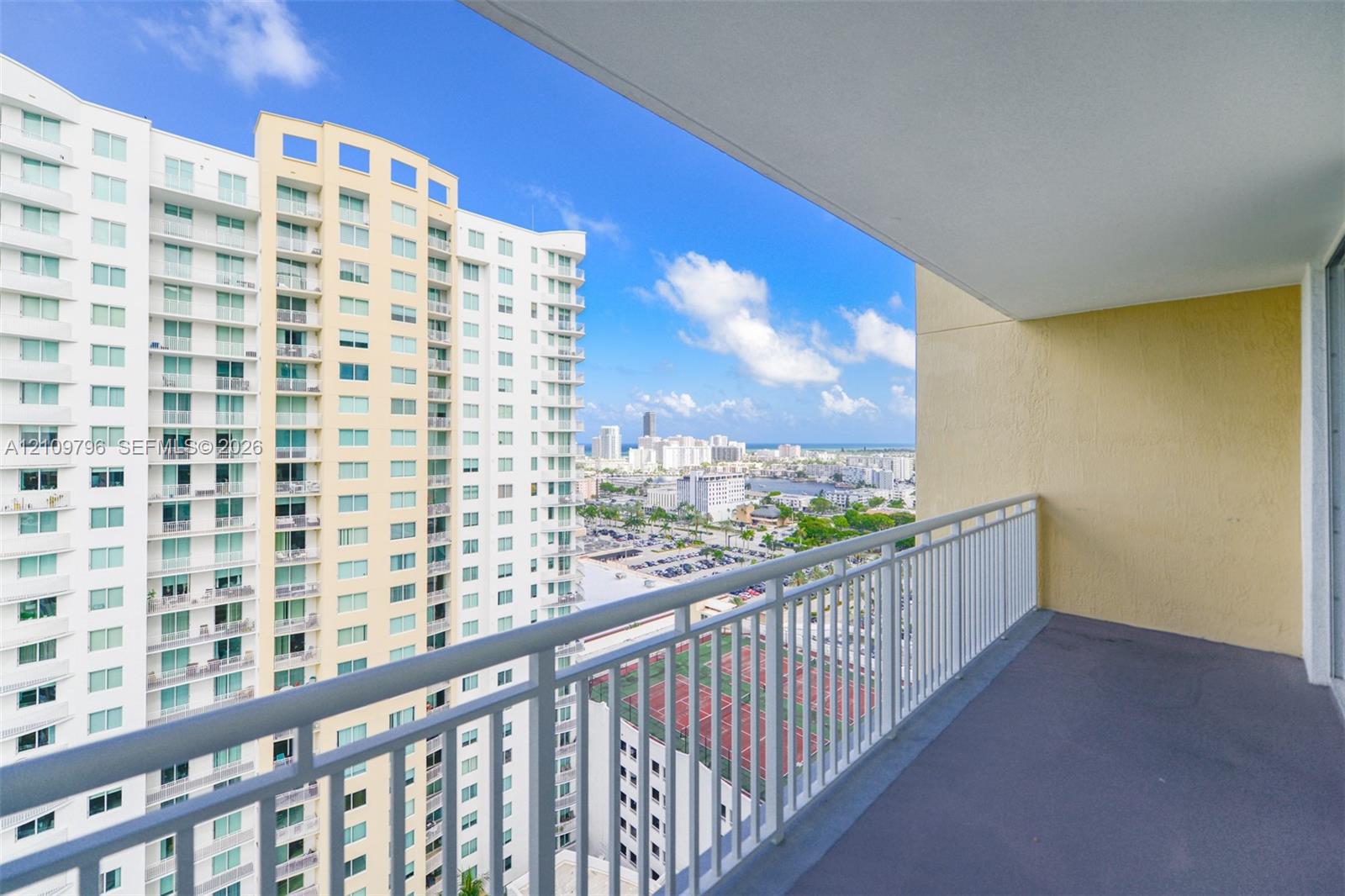 Covered balcony featuring a white metal railing, concrete flooring, and an expansive urban backdrop Covered balcony featuring a white metal railing, concrete flooring, and an expansive urban backdrop