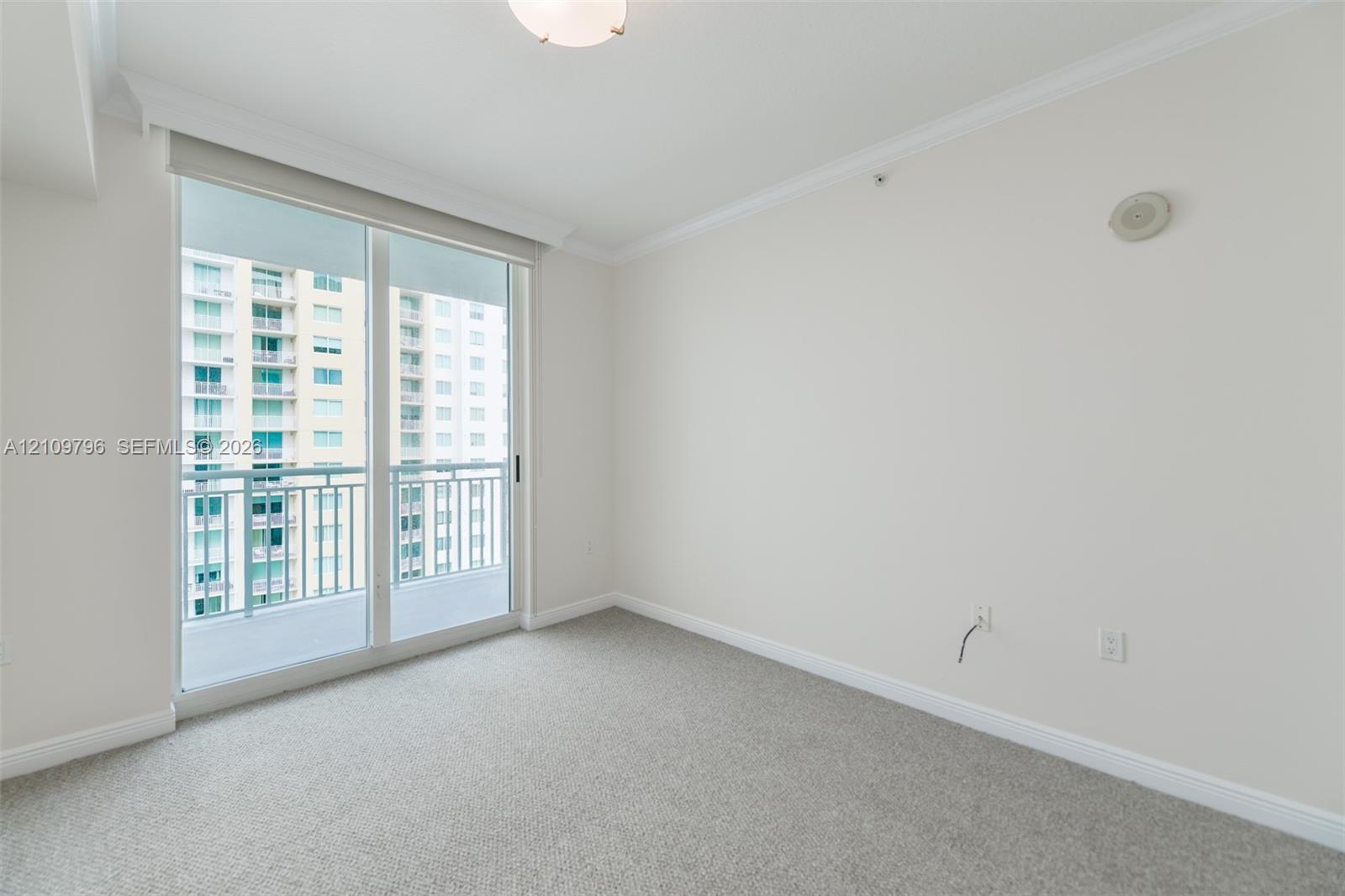 Neutral-toned interior featuring wall-to-wall carpeting, crown molding, and a sliding glass door providing access to a private balcony