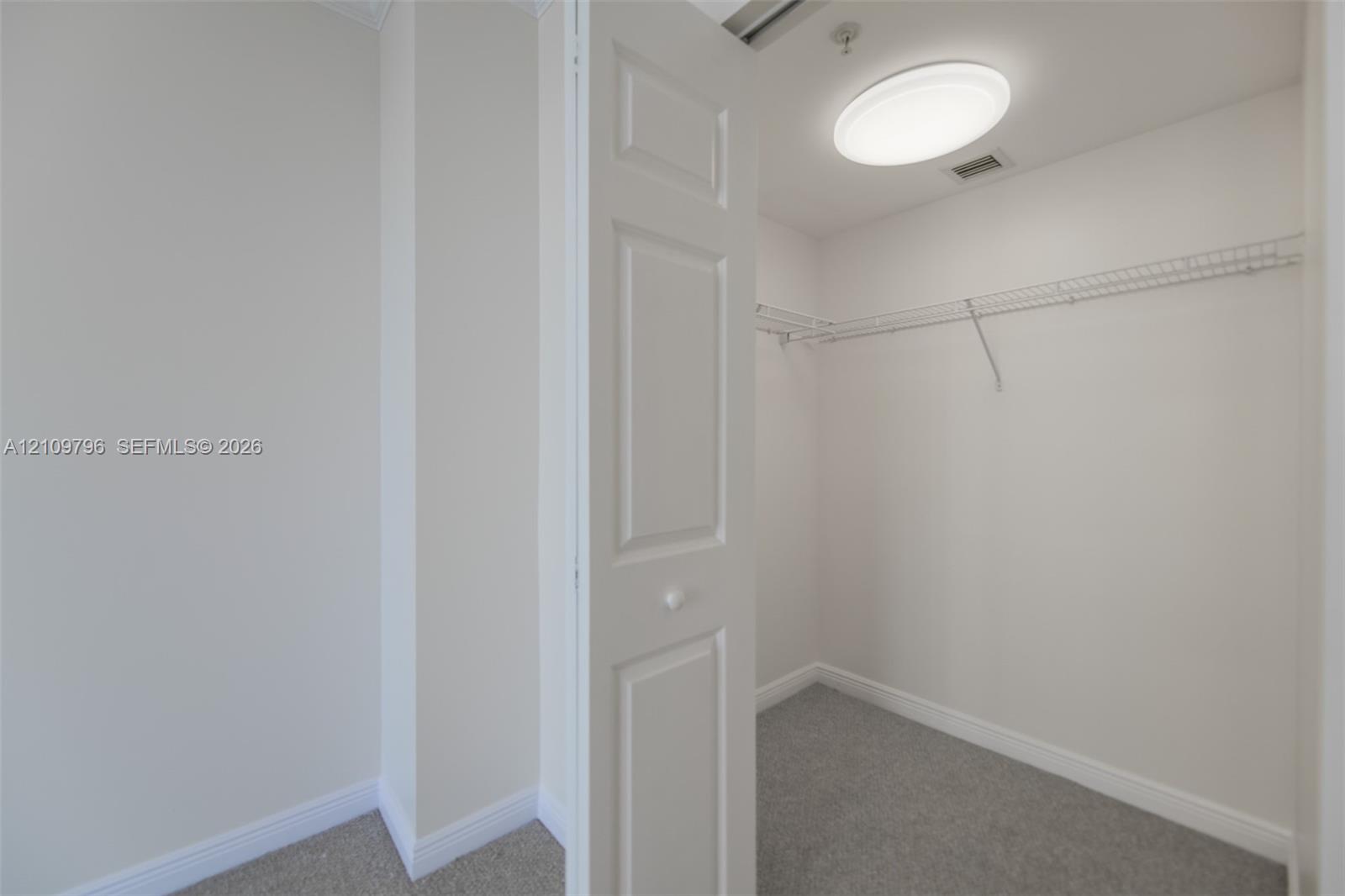 Walk-in closet featuring carpeted flooring, white paneled bifold doors, and wire shelving Walk-in closet featuring carpeted flooring, white paneled bifold doors, and wire shelving
