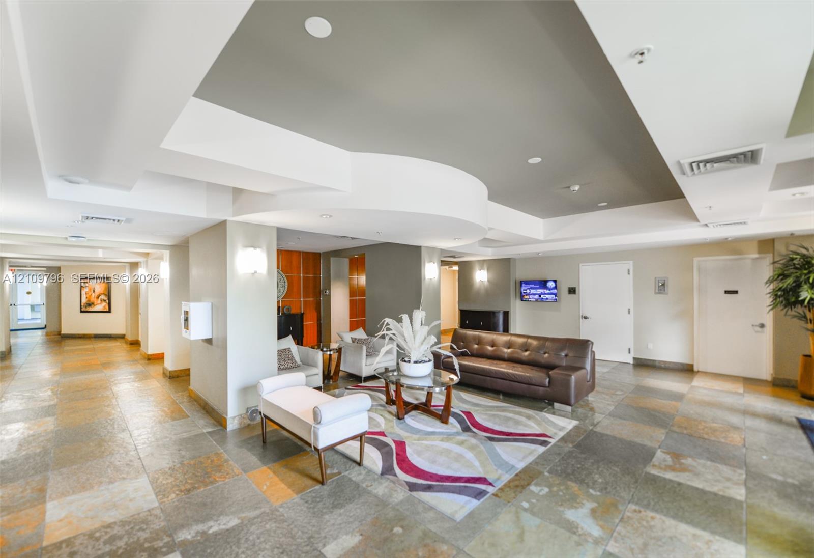 Grand lobby featuring coffered ceilings, multi-tonal stone tile flooring, wall-mounted sconce lighting, and decorative wood-panel accent wall