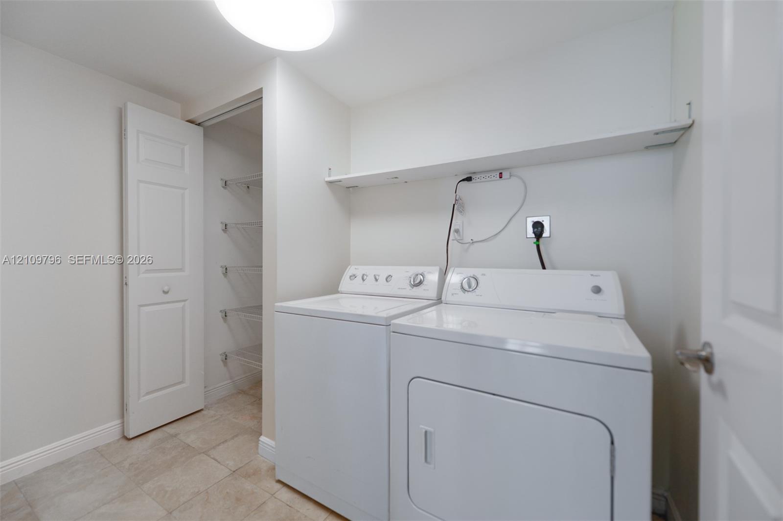 Laundry space featuring tile flooring, built-in wire shelving, and an overhead storage ledge Laundry space featuring tile flooring, built-in wire shelving, and an overhead storage ledge