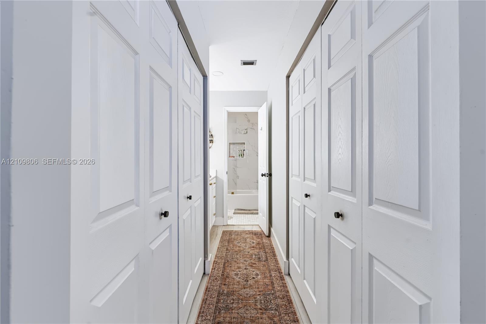 Hallway featuring dual sets of white paneled bifold closet doors with matte black hardware