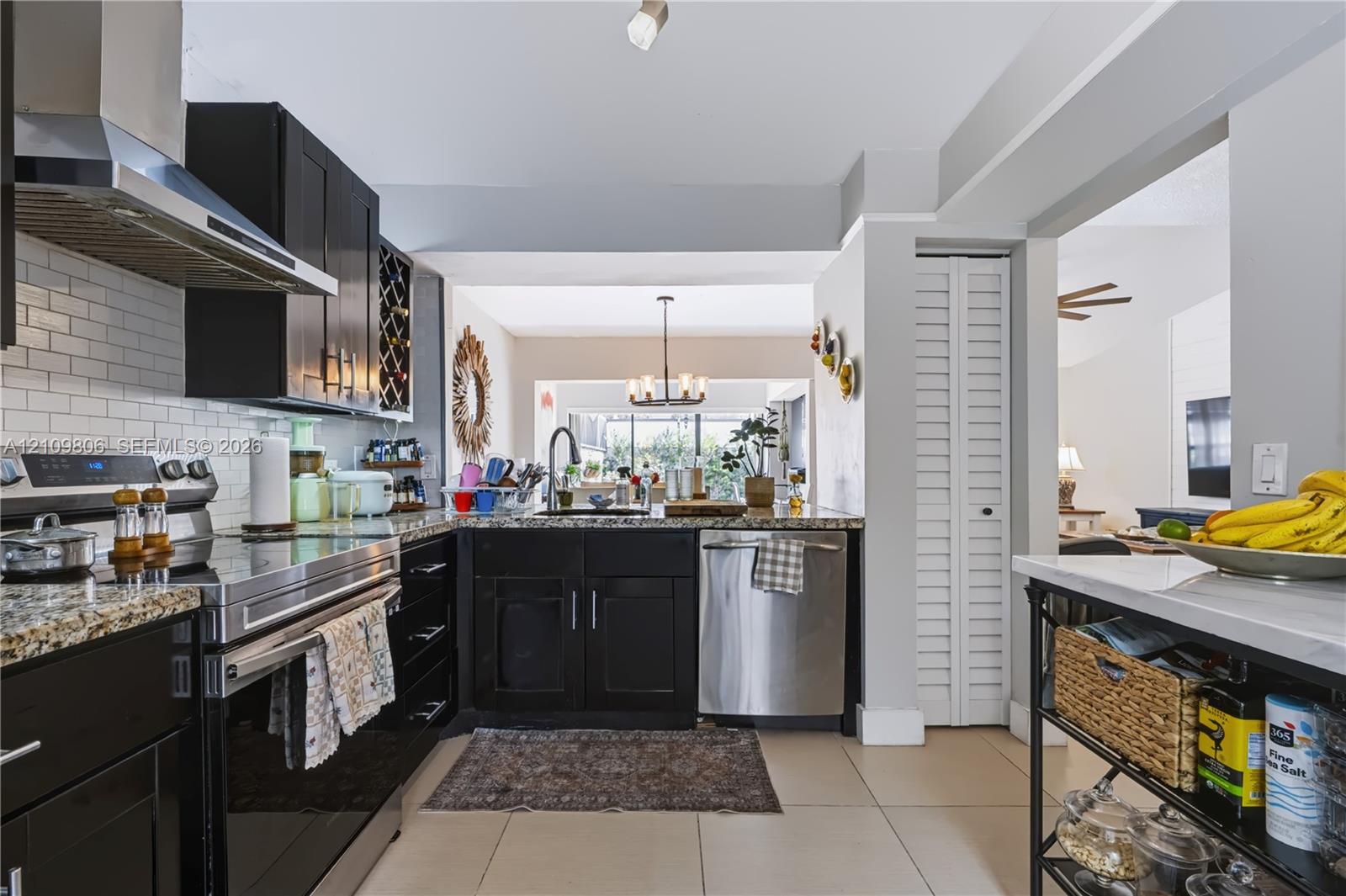 Kitchen featuring dark cabinetry, stone countertops, a stainless steel range hood, a subway tile backsplash, and ceramic tile flooring