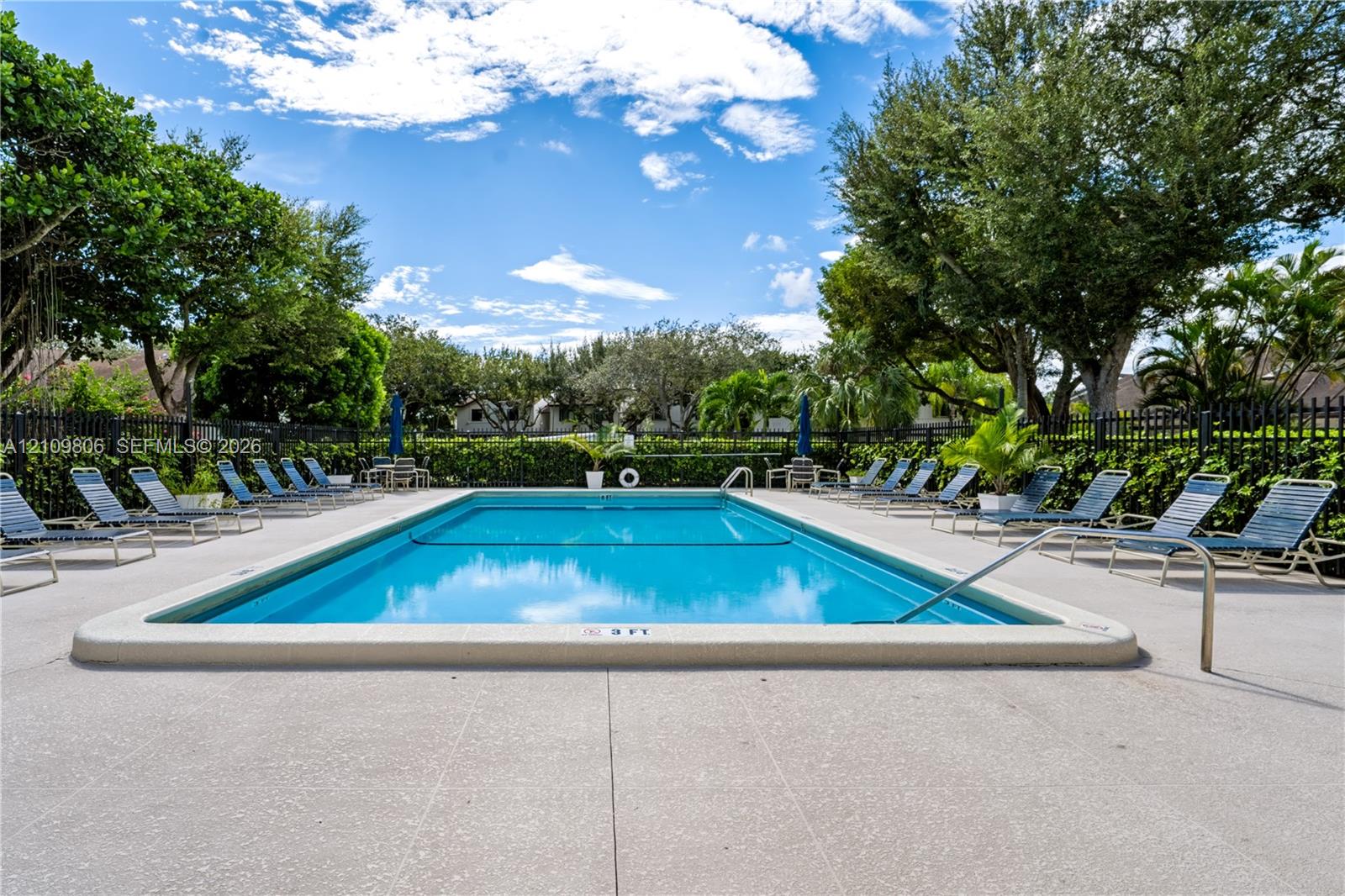 Rectangular swimming pool featuring a concrete deck and perimeter black metal fencing surrounded by mature landscaping