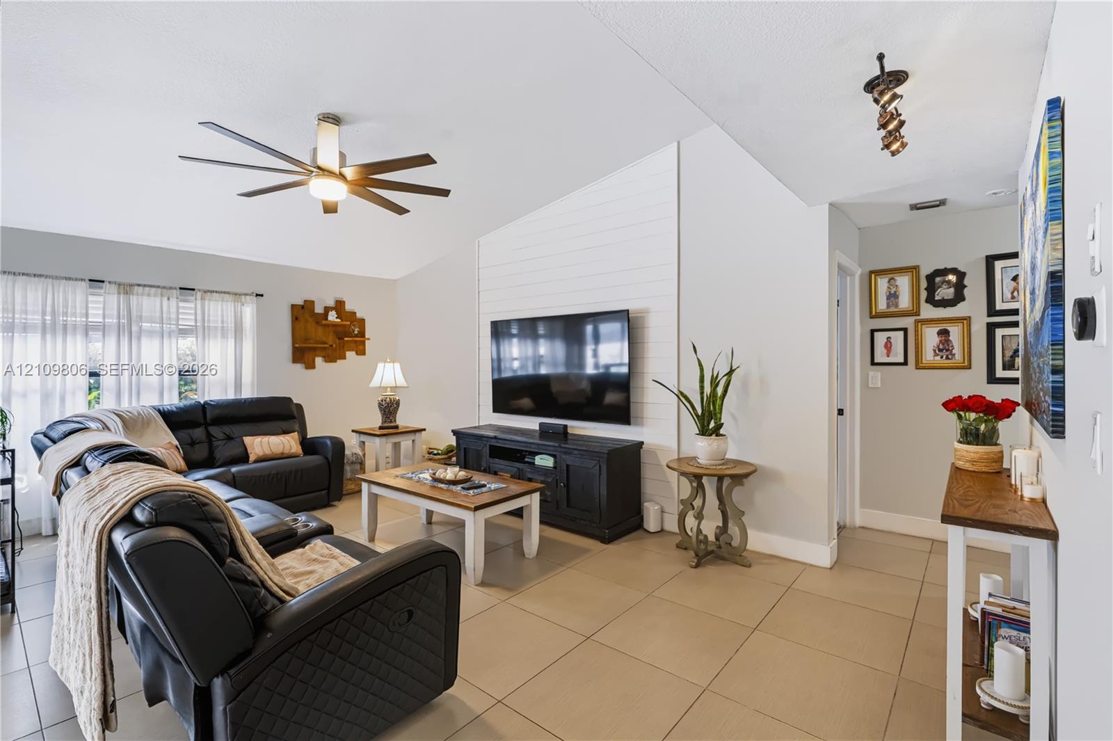 Living area featuring a vaulted ceiling, large-format tile flooring, shiplap accent wall, and a multi-blade ceiling fan