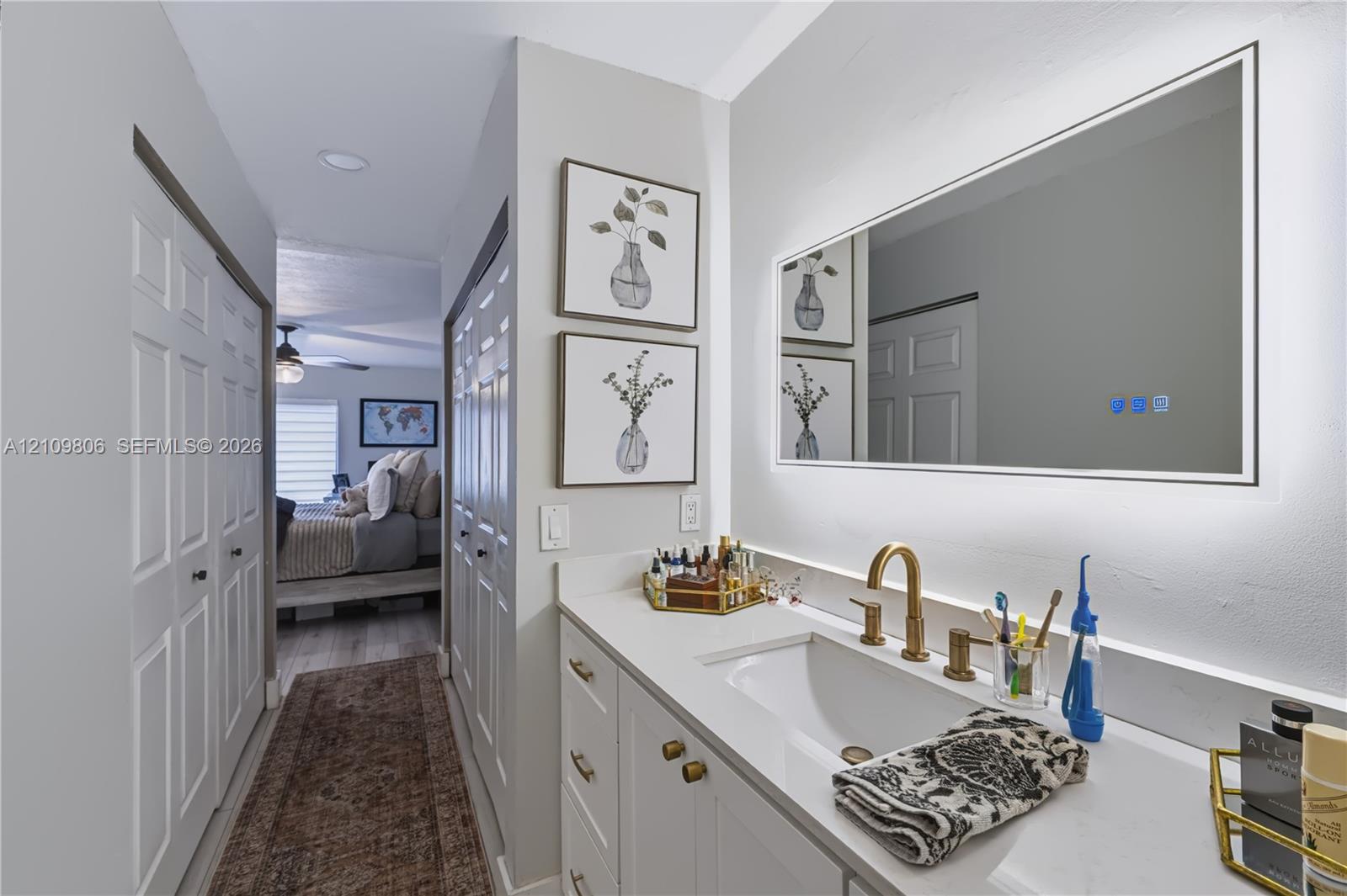 Bathroom vanity featuring white cabinetry, a solid surface countertop with an integrated basin, a gold-tone widespread faucet, and a large rectangular LED-backlit mirror