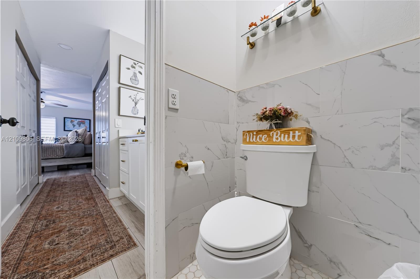 Half-bath featuring large-format white stone-finish wall tile, brass-finish hardware, hexagonal floor tile, and a glass-shelf vanity fixture