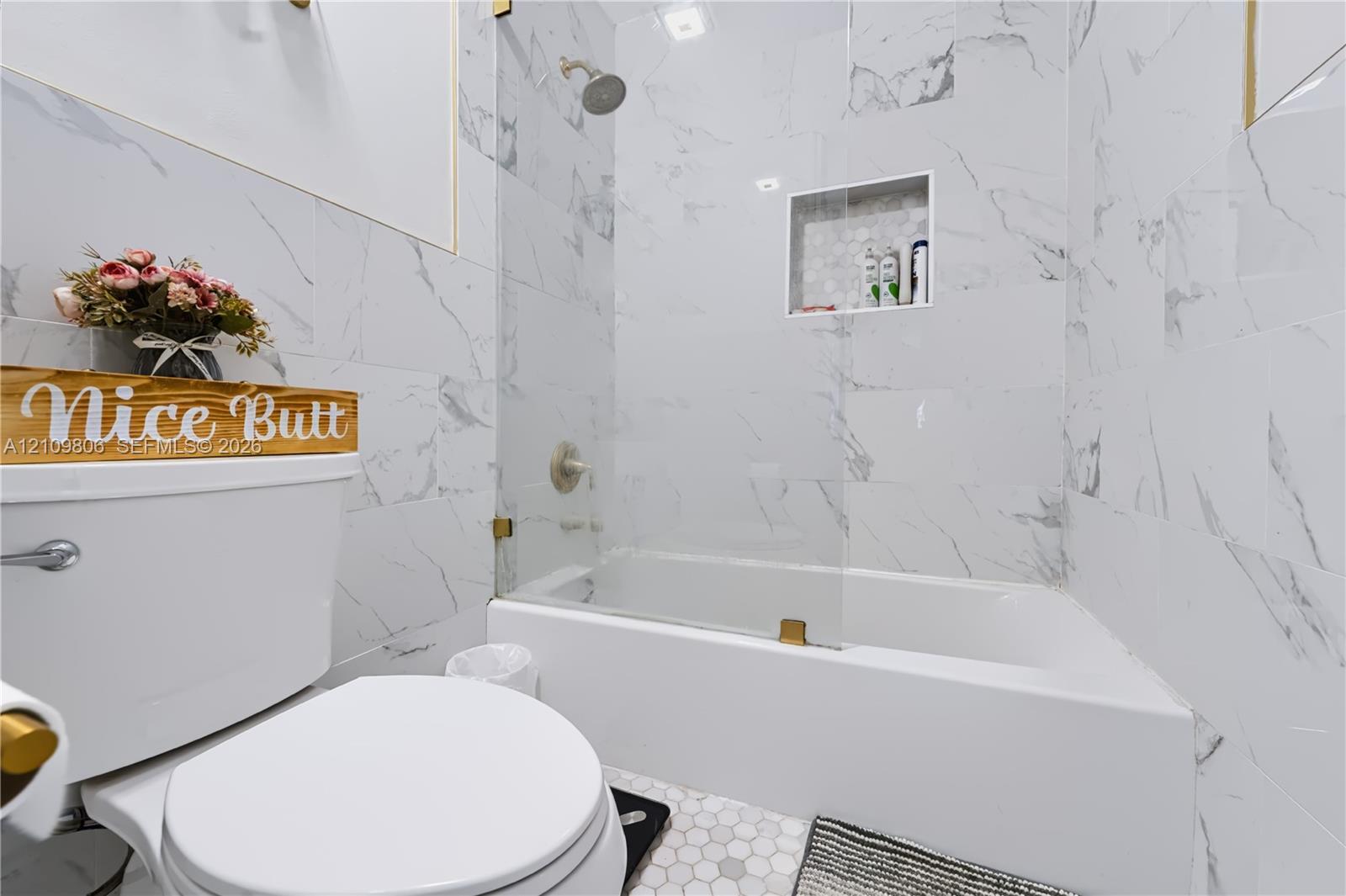 Full-height stone-look tile wall surround, glass partition, integrated built-in shower niche, and white porcelain fixtures