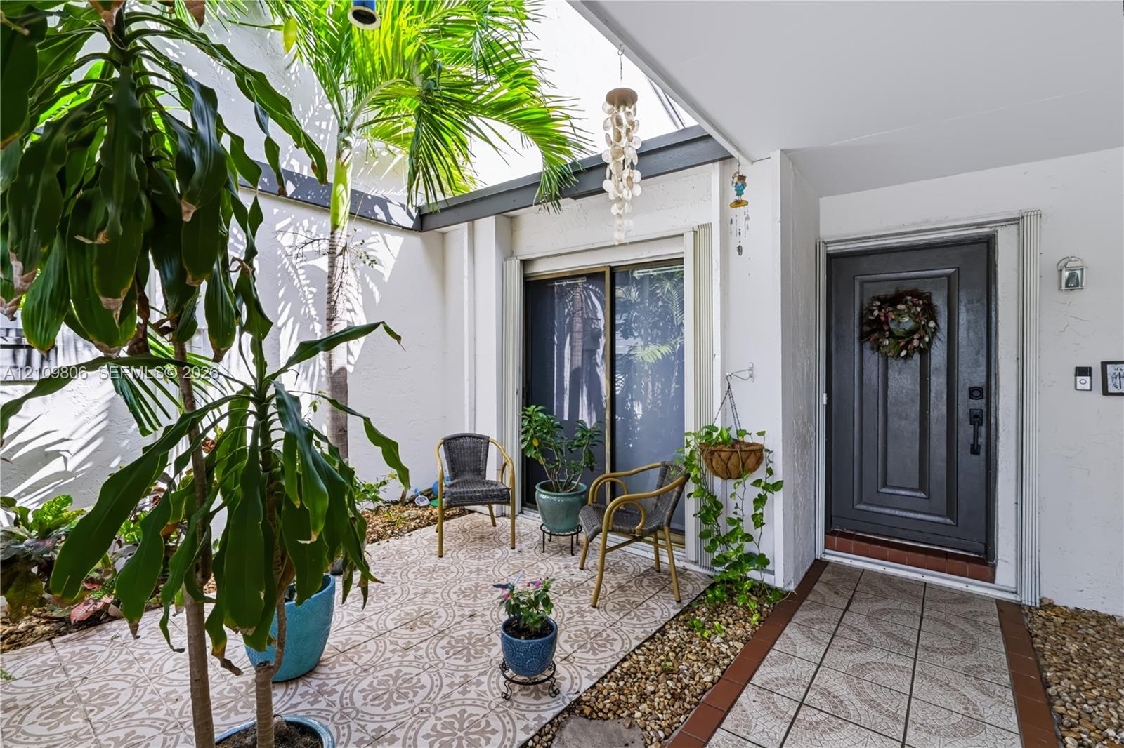 Enclosed courtyard featuring patterned tile flooring, exposed structural beams, gravel landscaping, and a solid-panel front entry door