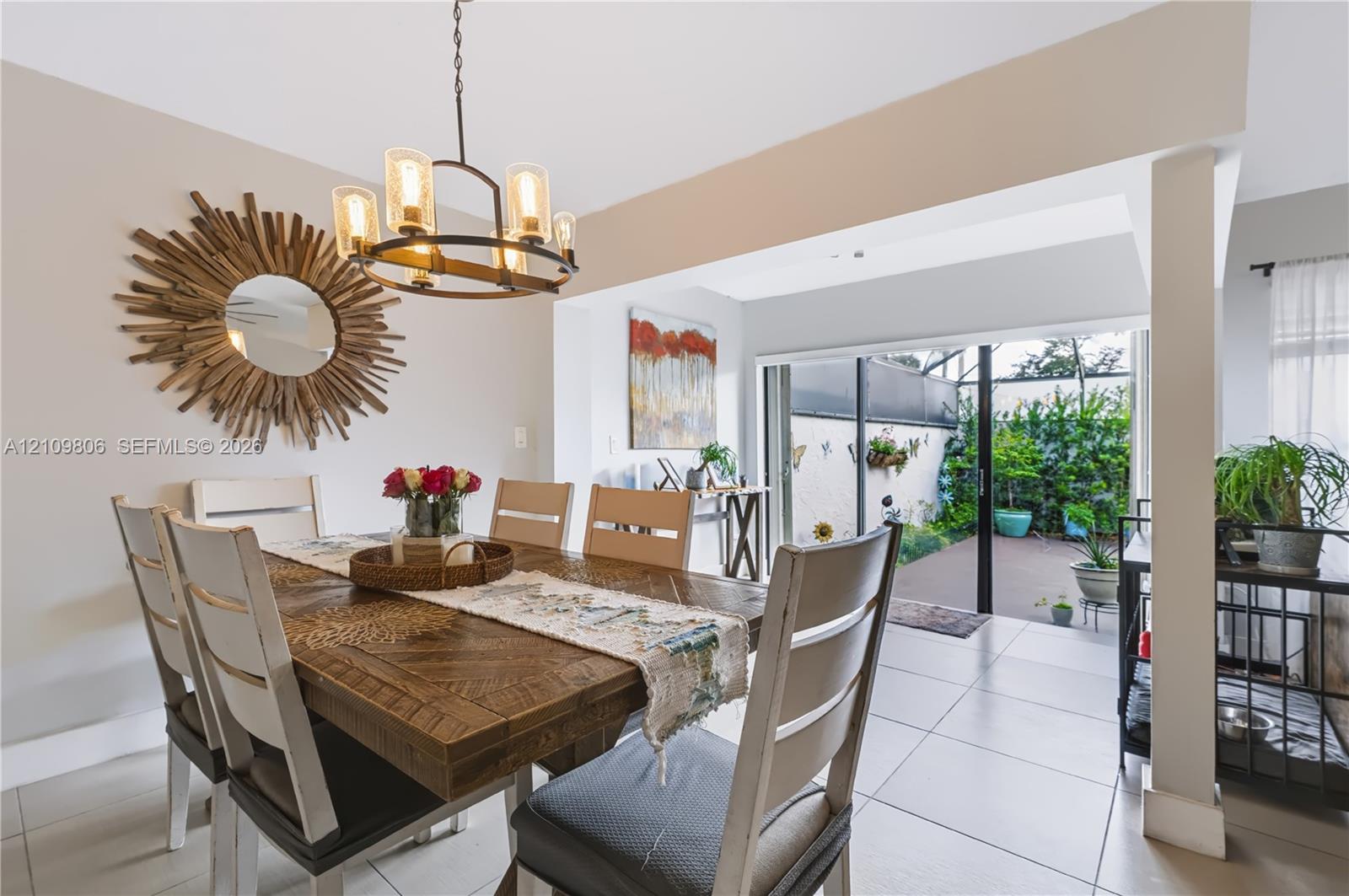 Dining area featuring large-format tile flooring, a circular multi-light chandelier, and sliding glass doors providing outdoor access to a private paved courtyard