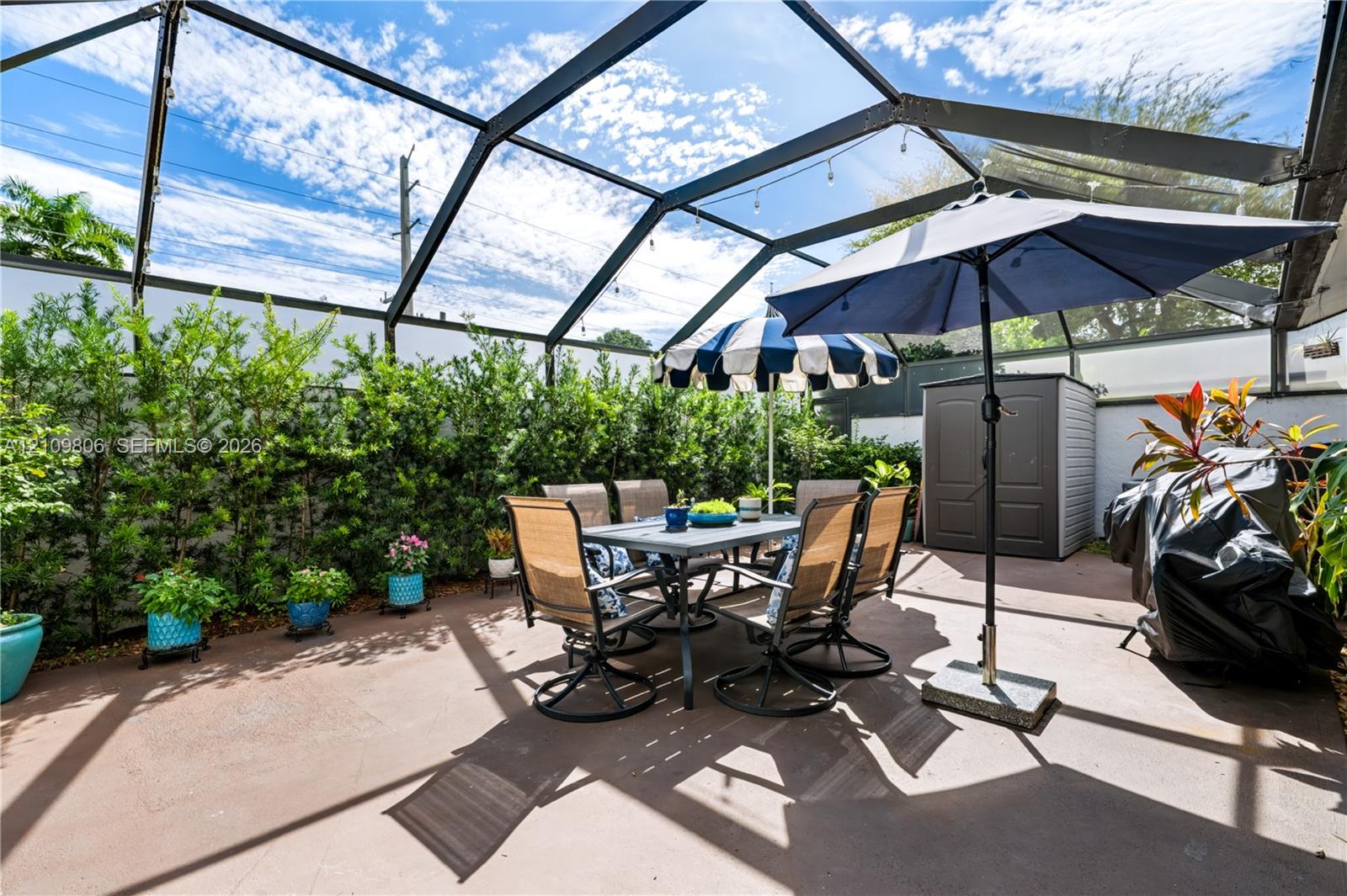 Screened-in outdoor patio featuring a concrete floor and a perimeter of dense, mature shrubbery